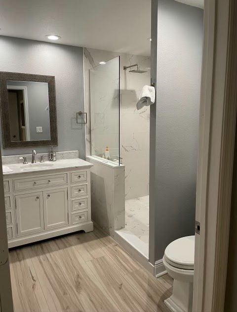 Modern bathroom with white vanity, mirror, tiled shower, and toilet beside a gray wall.