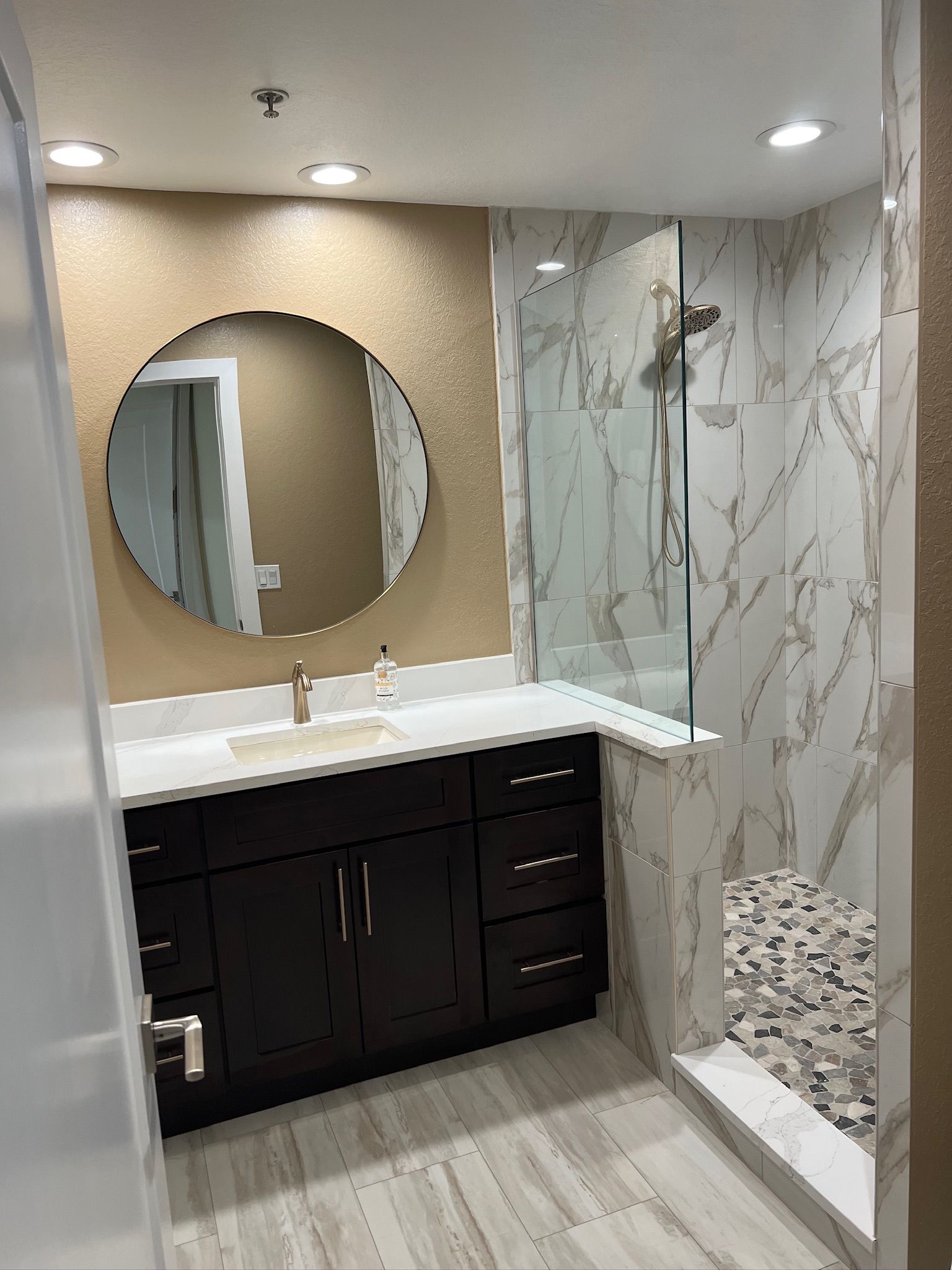 Modern bathroom with double vanity, round mirror, and marble-tile shower stall