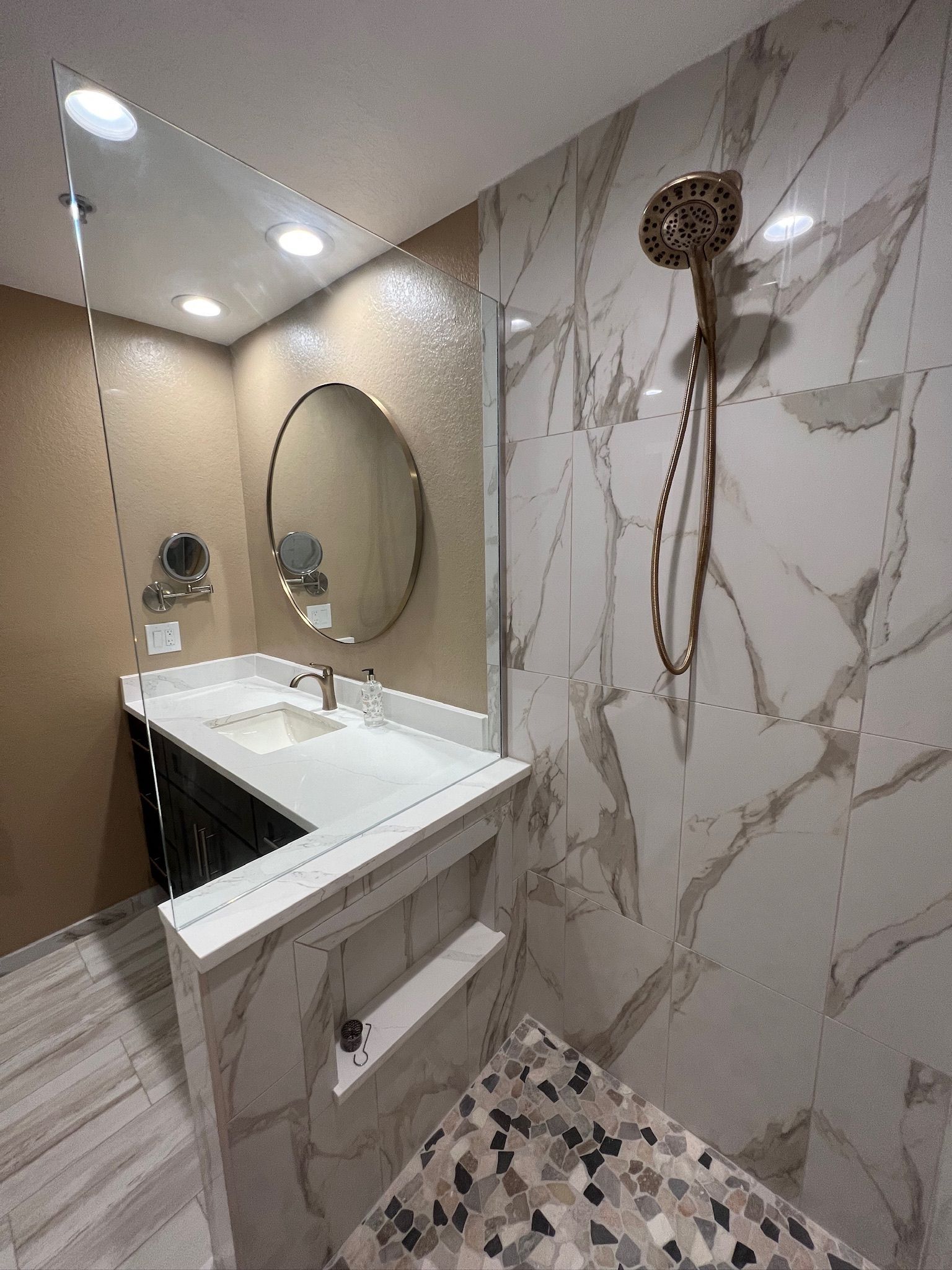 Modern bathroom with marble-pattern walls, a wall-mounted sink, mirror, and open shower area