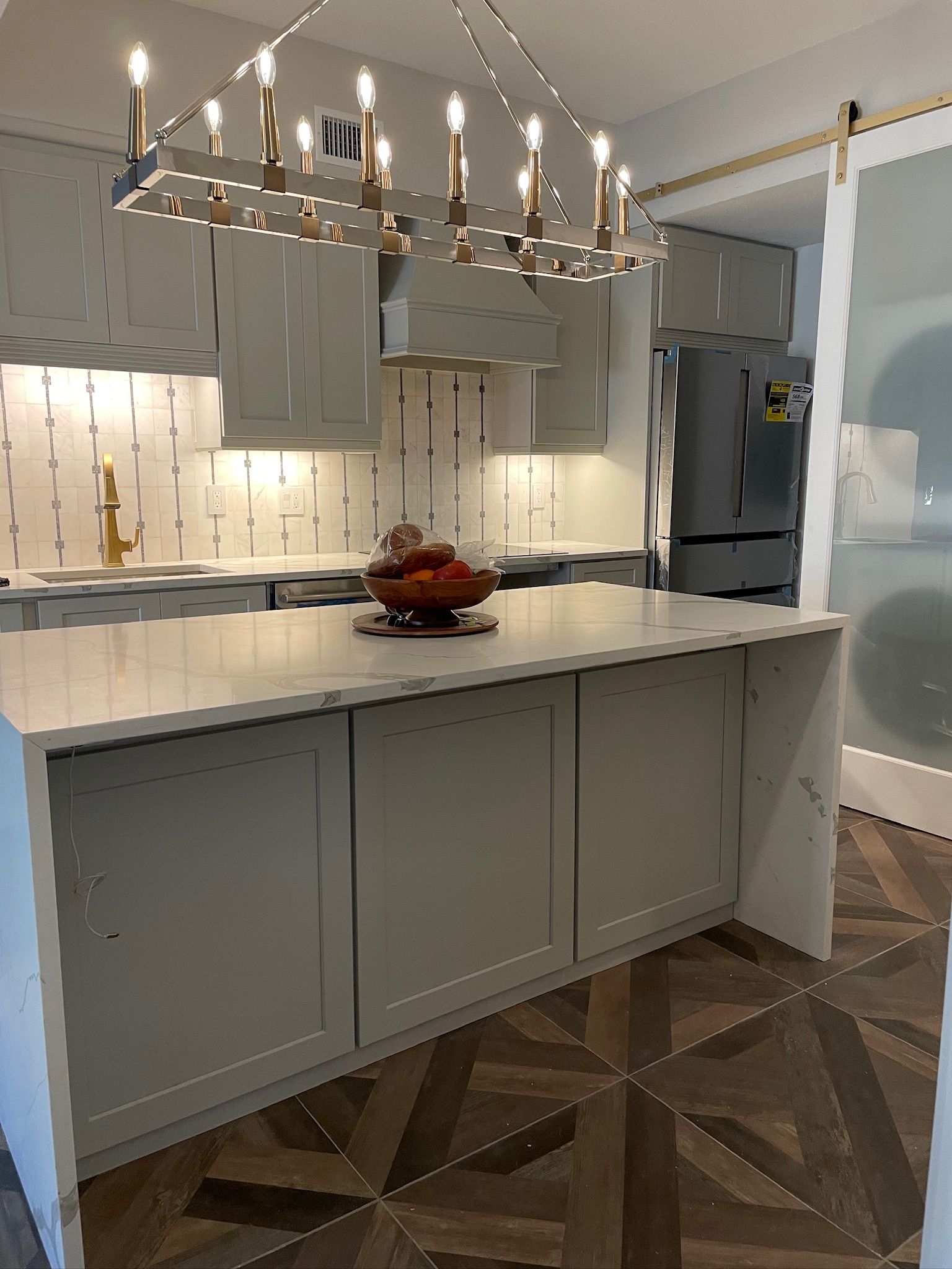 Modern kitchen with a white island, chandelier, gray cabinets, and patterned tile floor