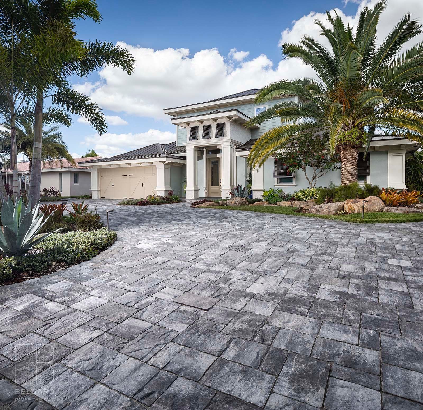 Modern white stucco house with stone driveway, palm trees, and landscaped front yard under a blue sky