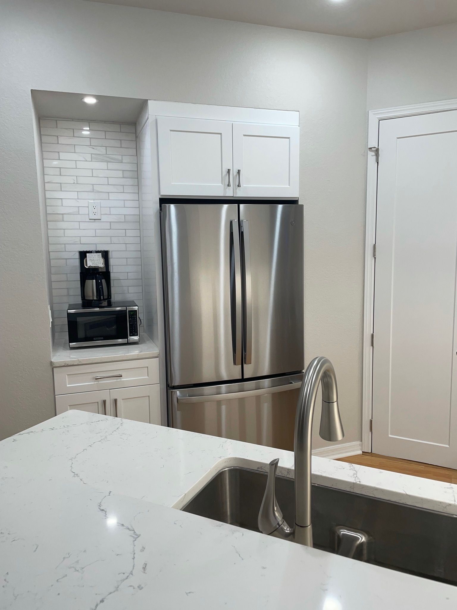 Modern kitchen with stainless steel refrigerator, white cabinets, and a sink island.