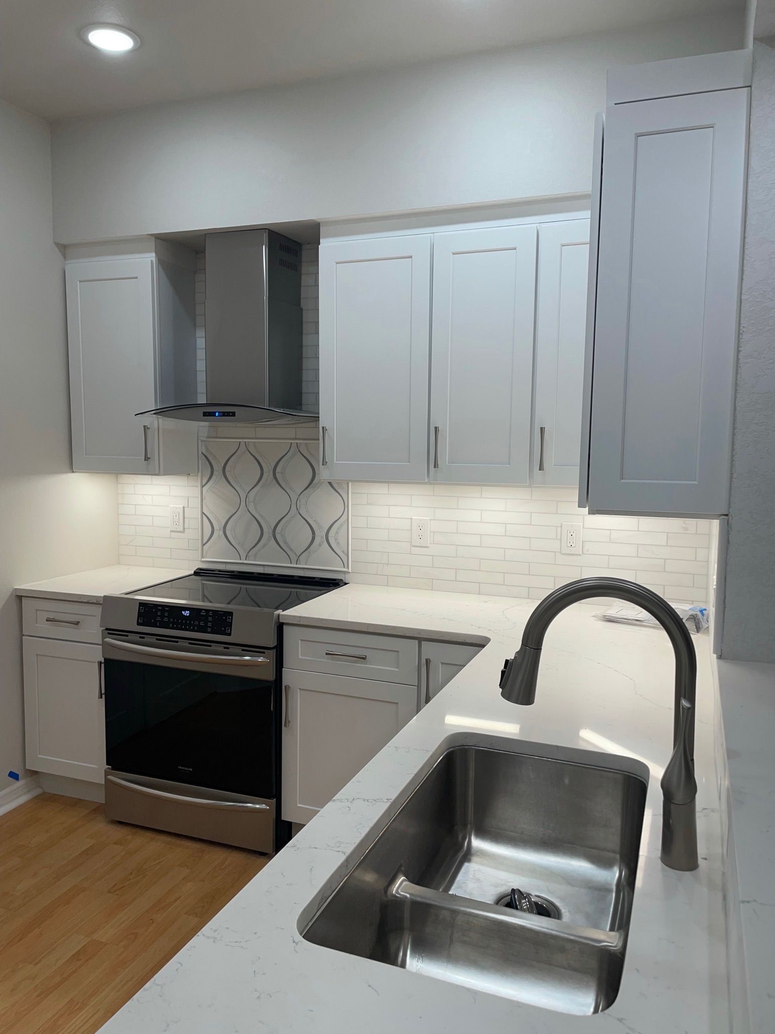 Modern white kitchen with stainless steel appliances, wood floor, and a double sink in the foreground