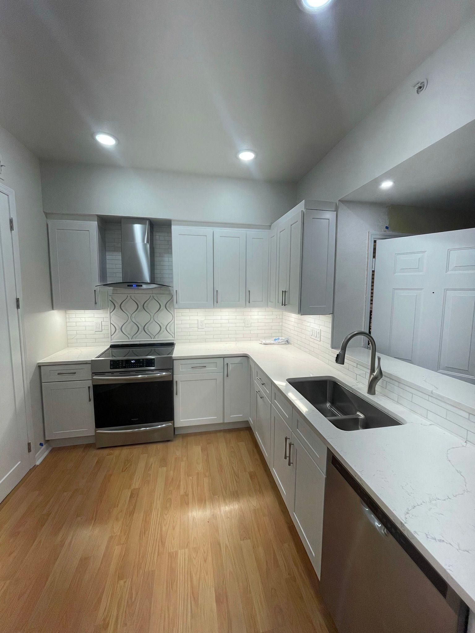 Bright modern kitchen with white cabinets, stainless stove, wood floor, and island sink.