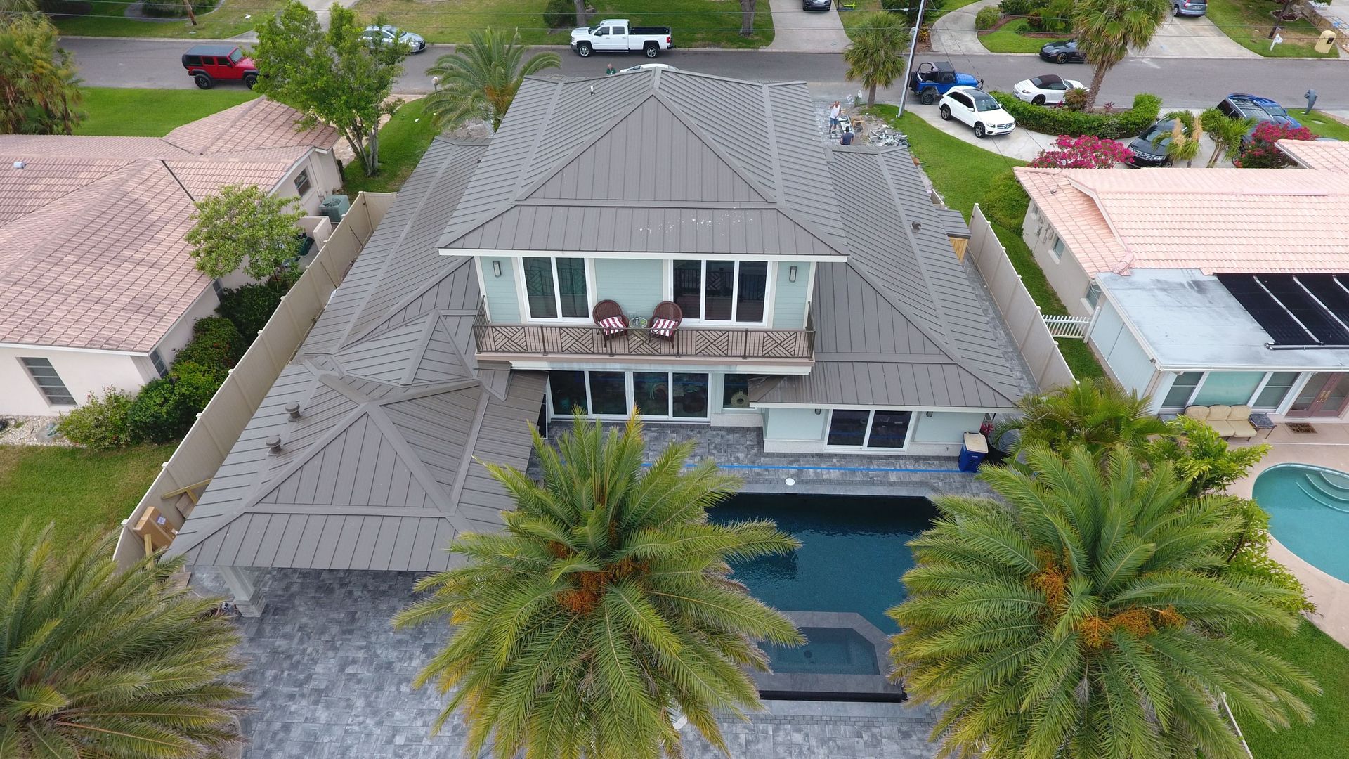 Aerial view of a house with a pool, palm trees, and a gray roof in a residential neighborhood.