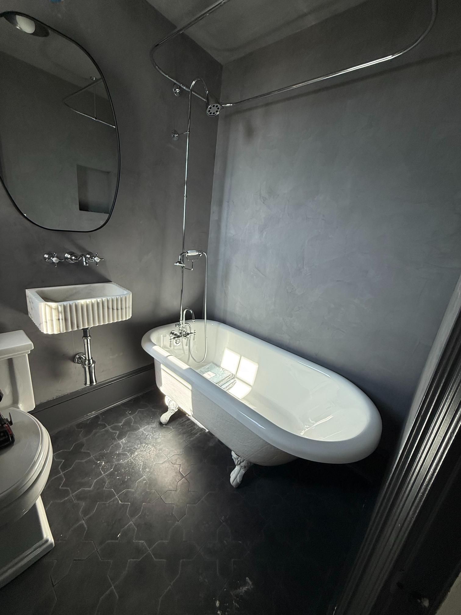 Small gray bathroom with a white clawfoot tub, sink, toilet, and dark tiled floor.