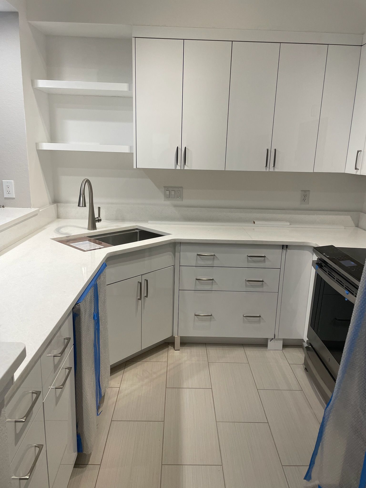 White U-shaped kitchen with cabinets, countertop, sink, and black appliances; some edges are taped off for work