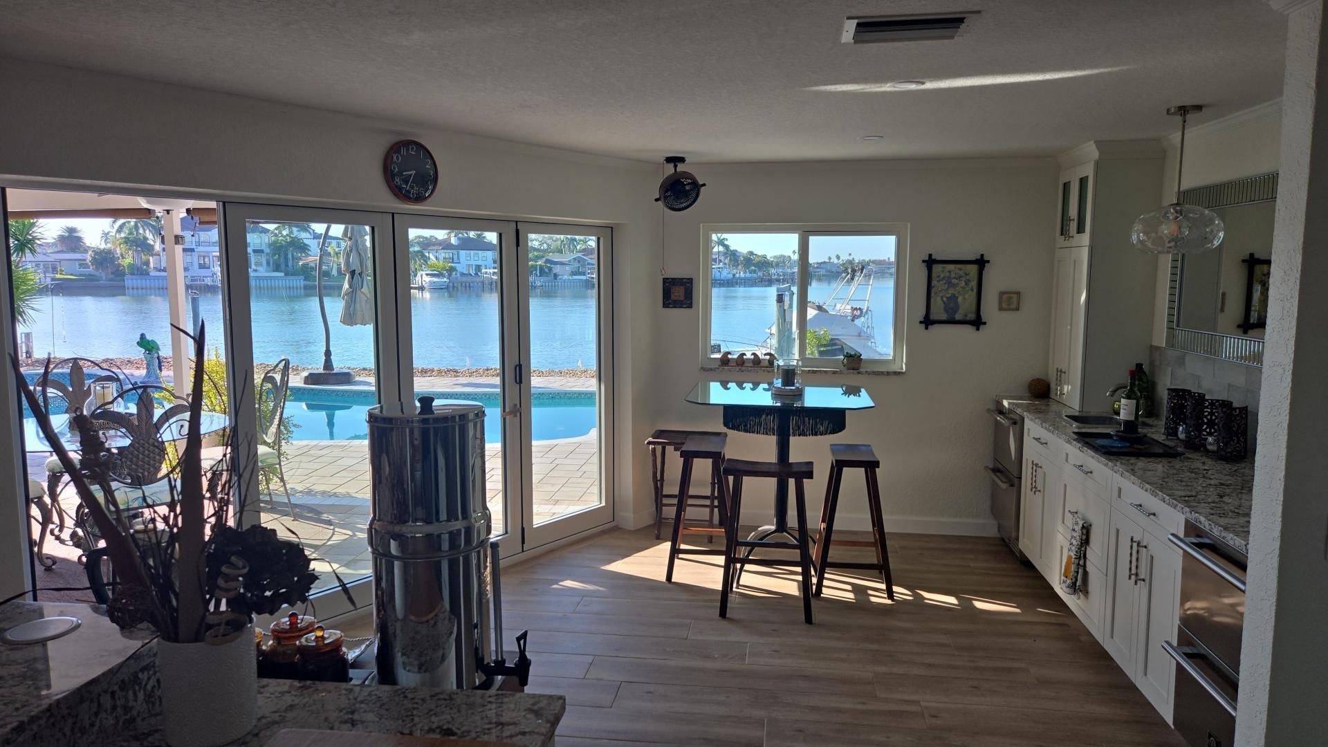 Bright kitchen and dining area with large windows overlooking a sunny waterfront.