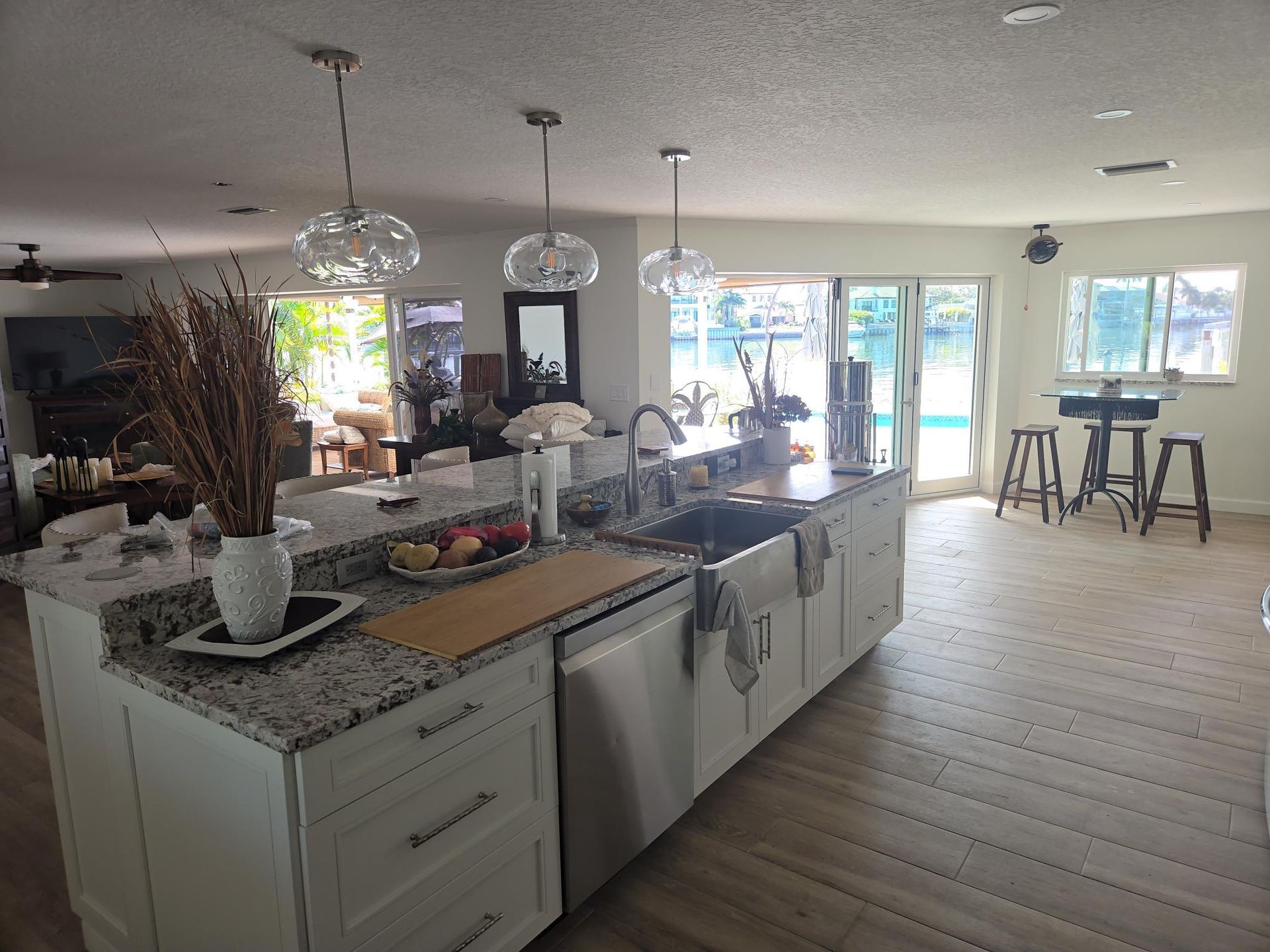 Bright open kitchen and dining area with white cabinets, granite island, pendant lights, and large windows