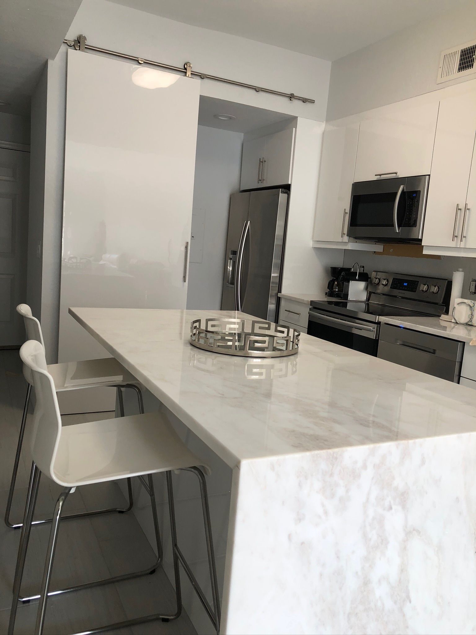 Modern kitchen with marble island, white cabinets, bar stools, and stainless steel appliances.