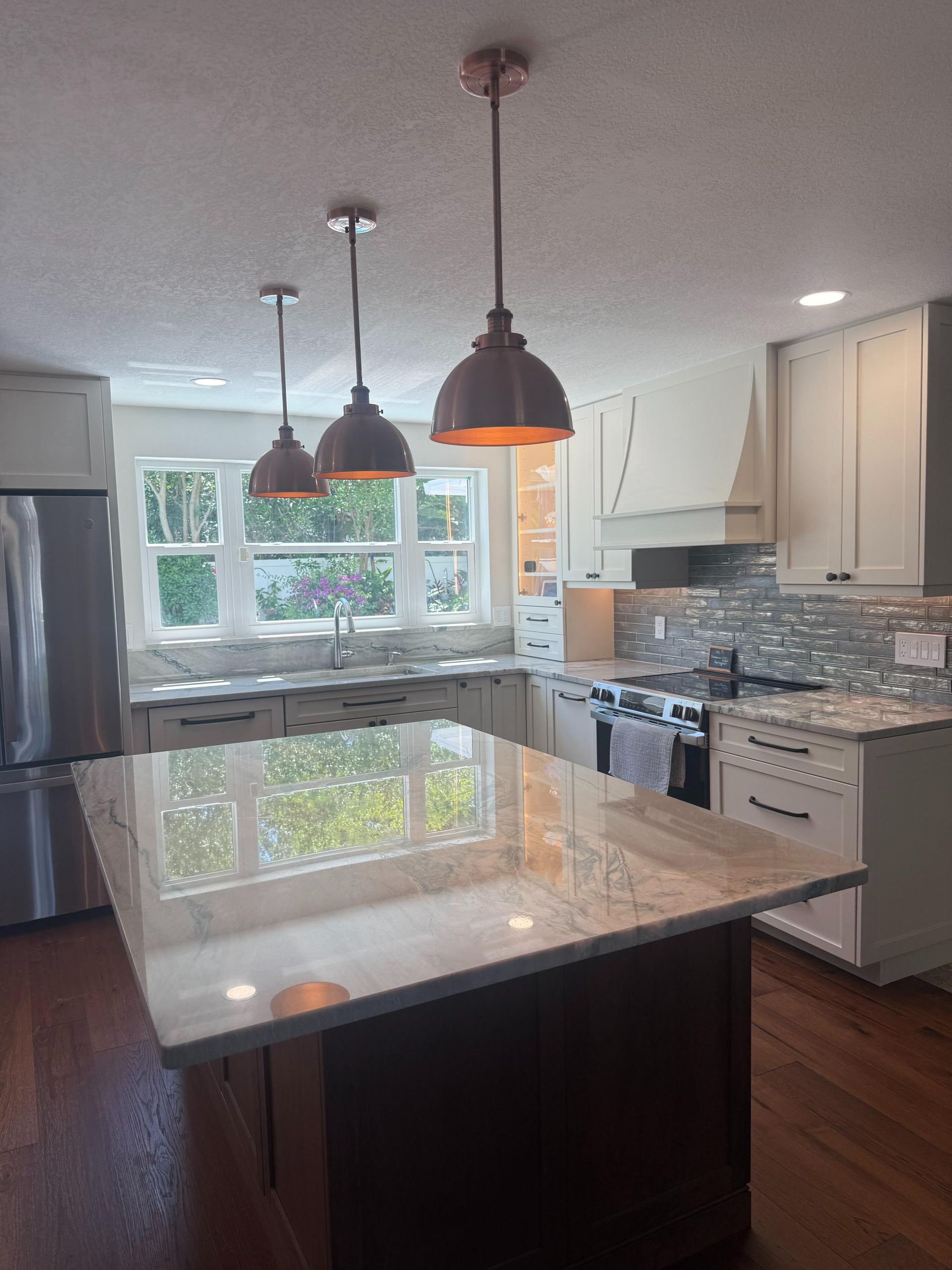 Modern kitchen with island, pendant lights, white cabinets, and large window over a sink.