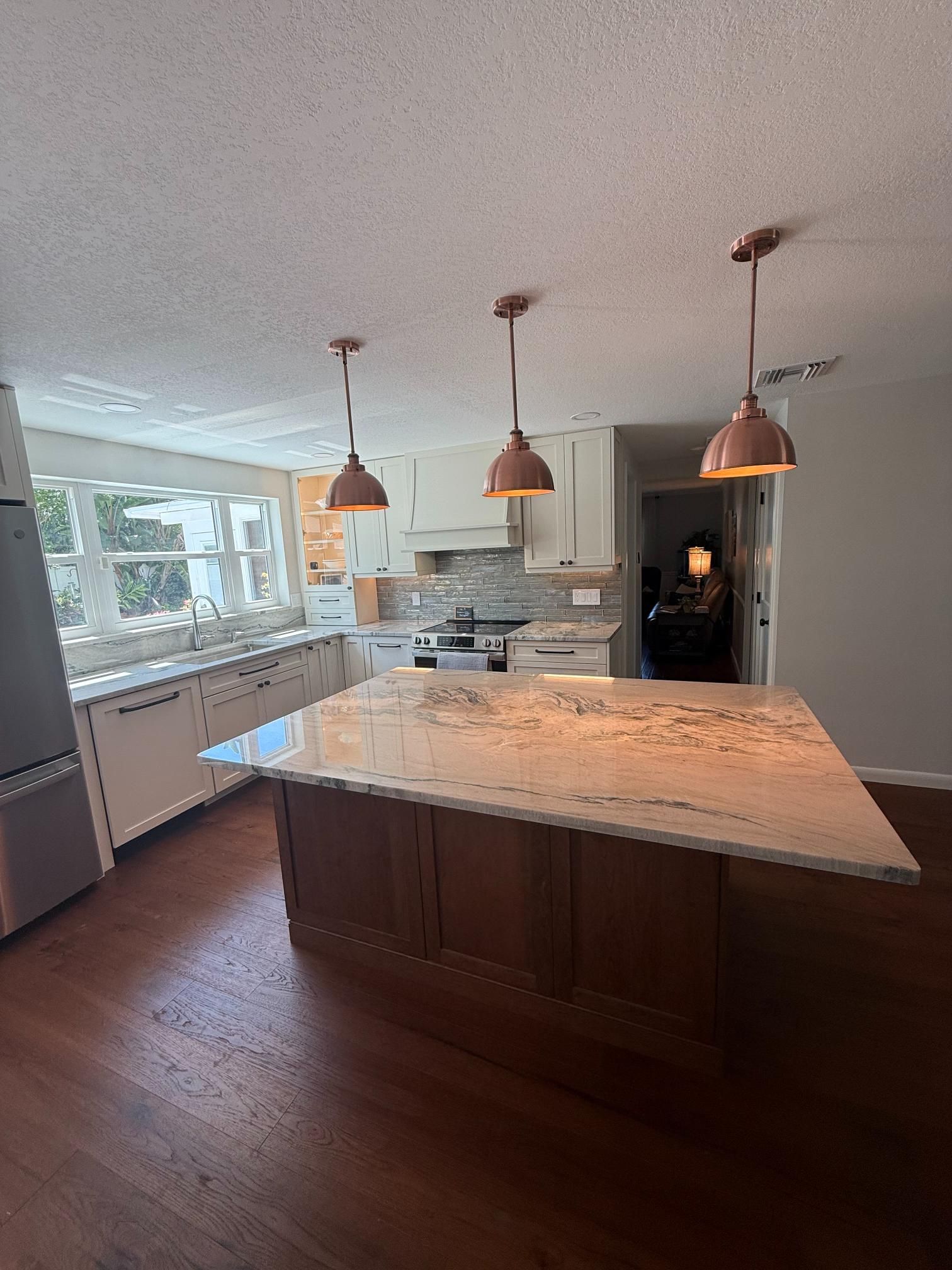 Modern kitchen with large island, white countertops, pendant lights, and hardwood floors