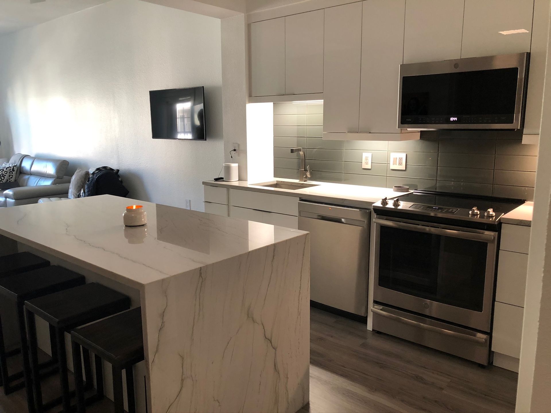 Bright modern kitchen with white cabinets, stainless appliances, and a marble island beside a living area