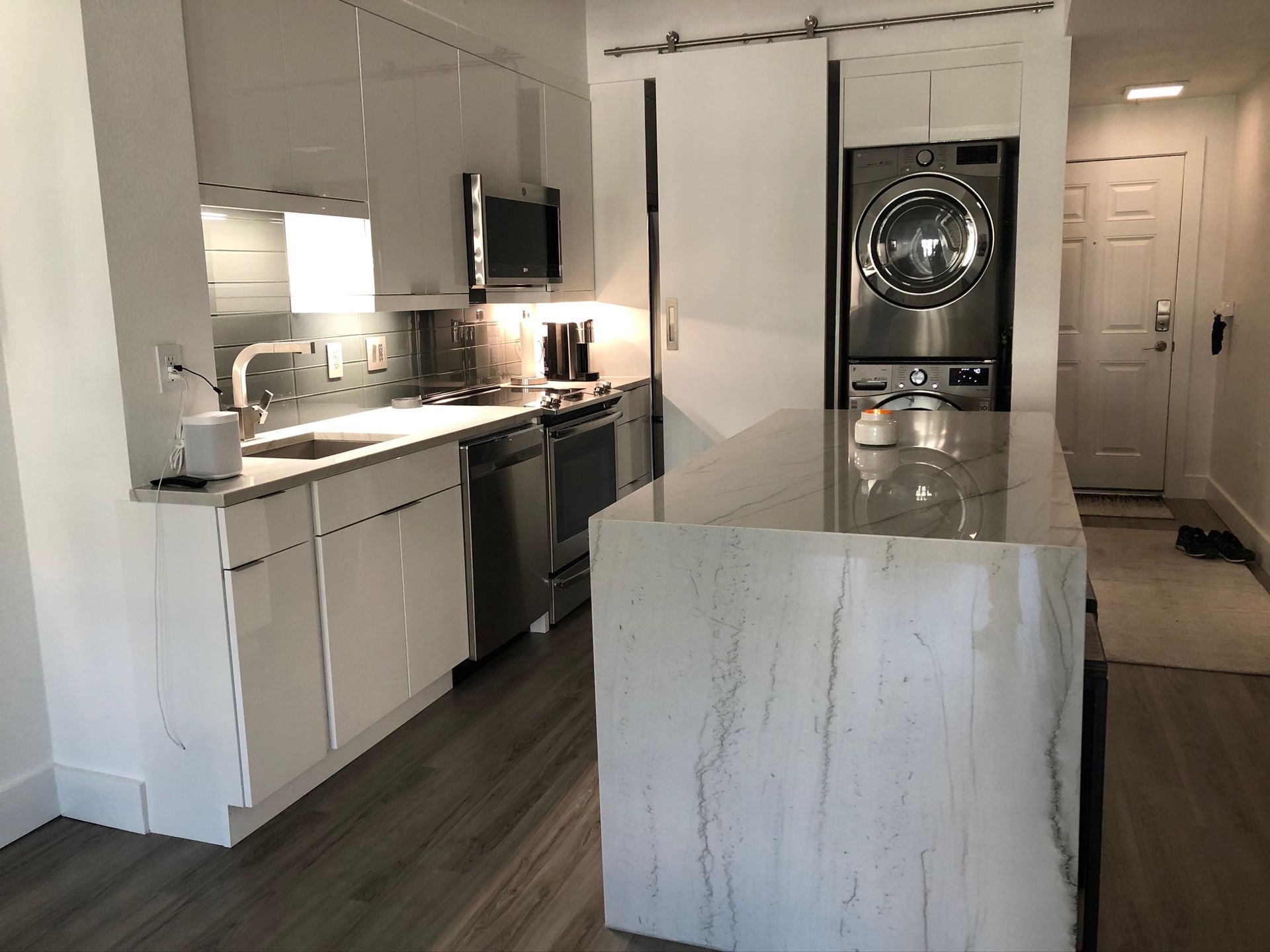 Modern kitchen with white cabinets, marble island, dark wood floor, and stacked washer/dryer in the back.