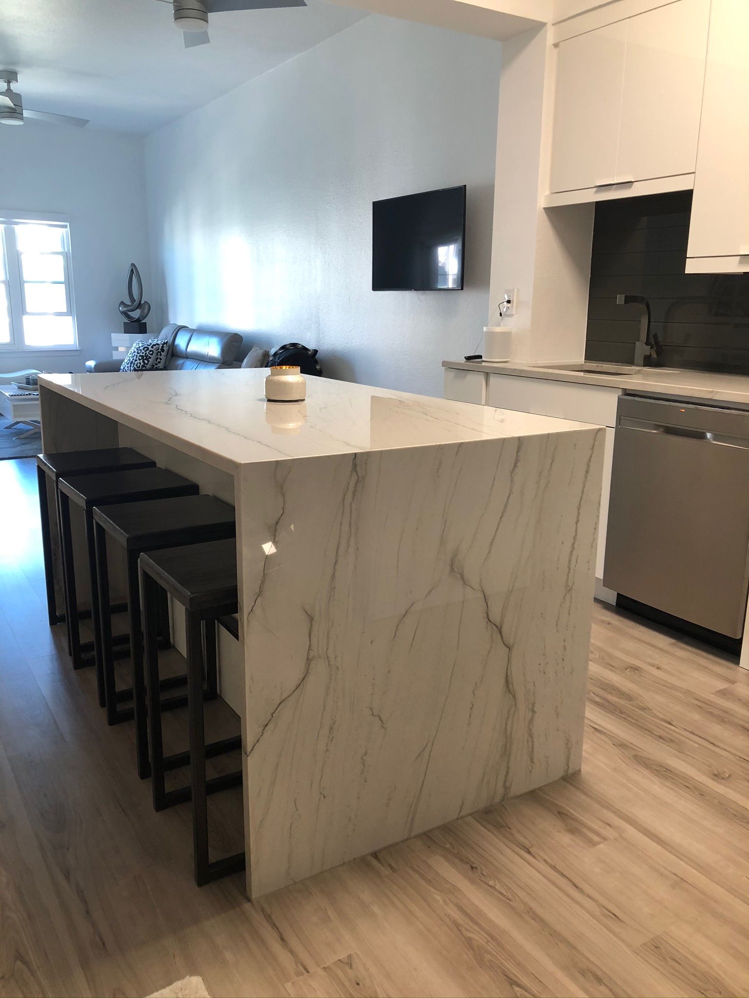 Modern kitchen with marble island, black bar stools, stainless appliances, and wall-mounted TV