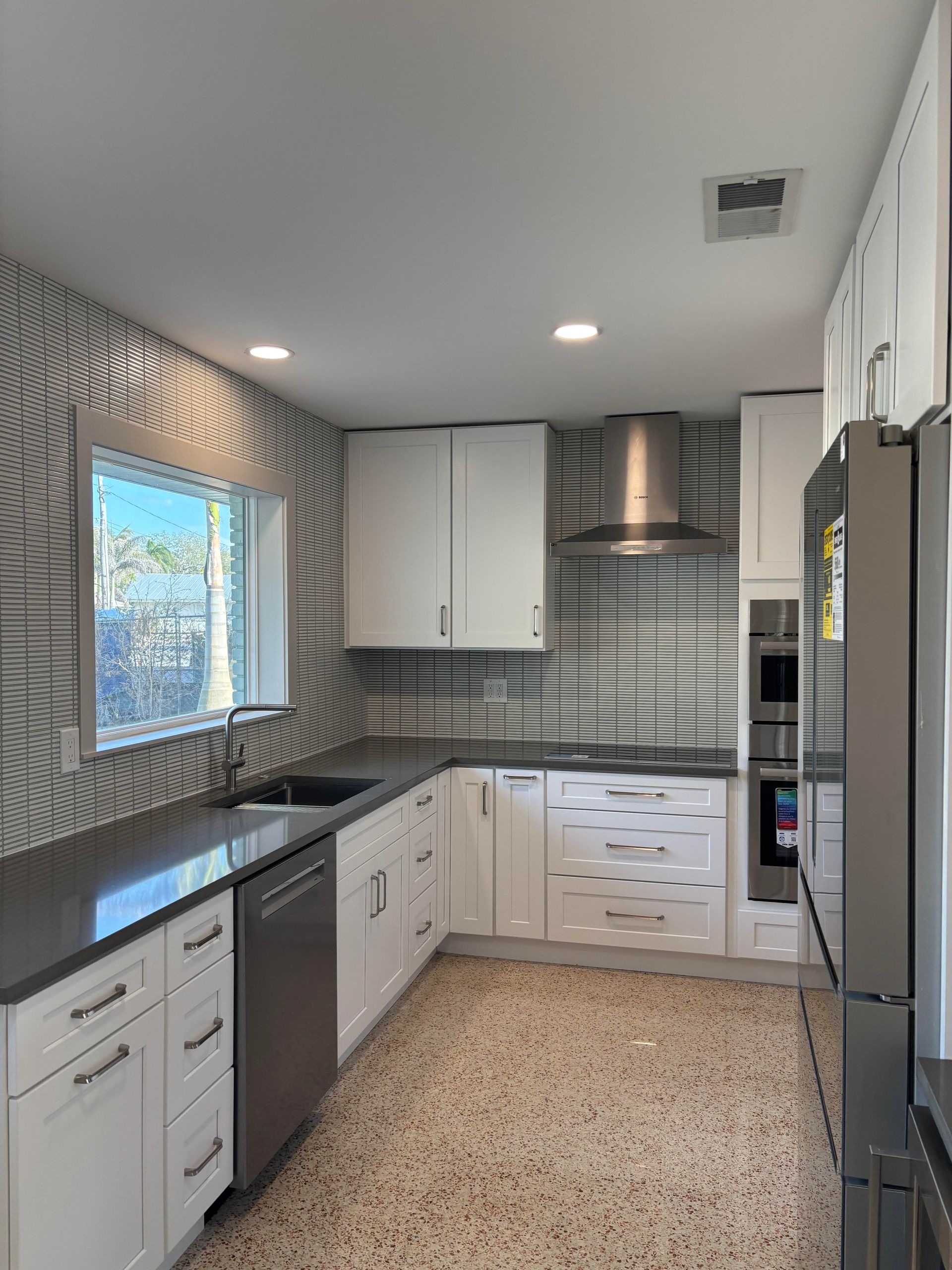 Modern kitchen with white cabinets, dark countertops, stainless steel appliances, and patterned backsplash.