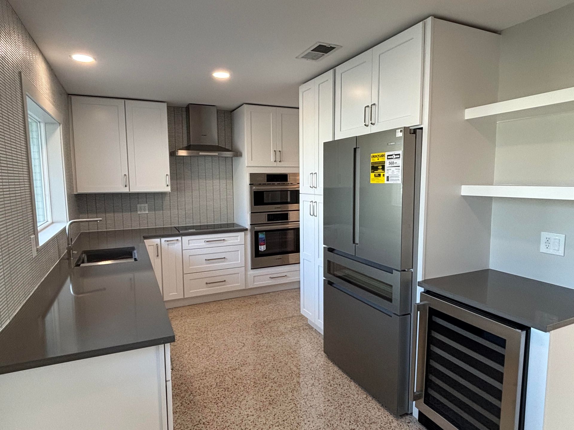 Modern kitchen with white cabinets, gray countertops, stainless steel appliances, and terrazzo flooring.
