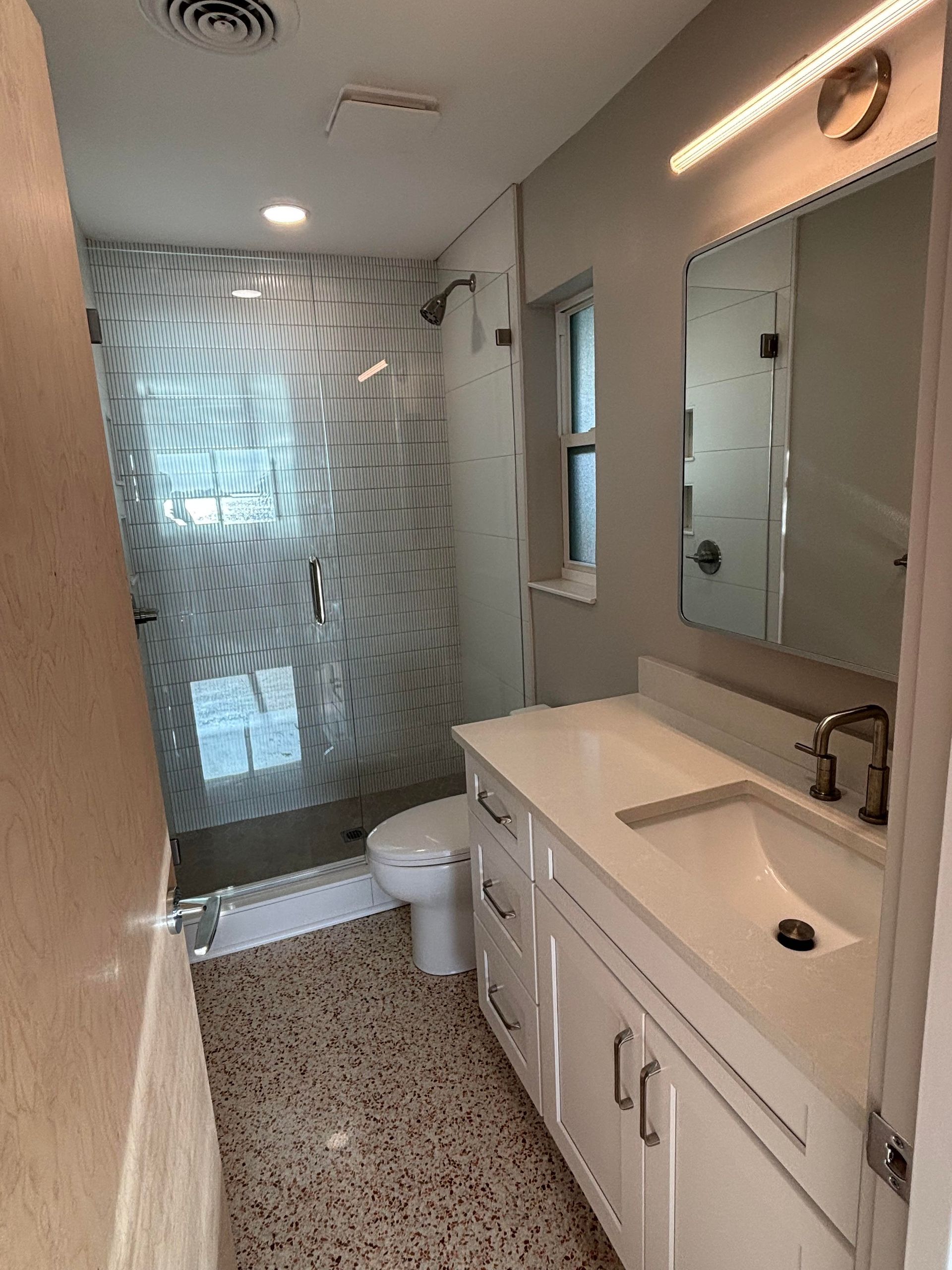 Modern bathroom with white vanity, patterned shower wall, and terrazzo floor.