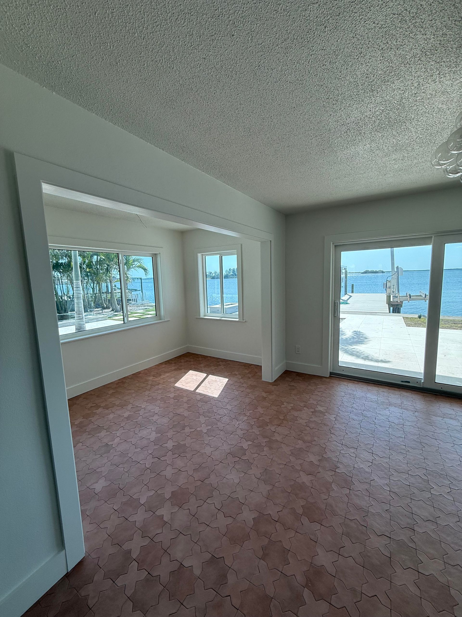 An empty room with cork flooring, windows facing a waterfront, and sliding glass door leading to a patio.