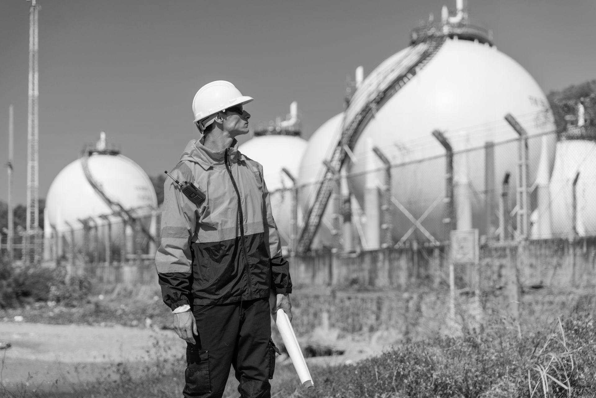Engineer in hard hat and work jacket surveys gas storage tanks.