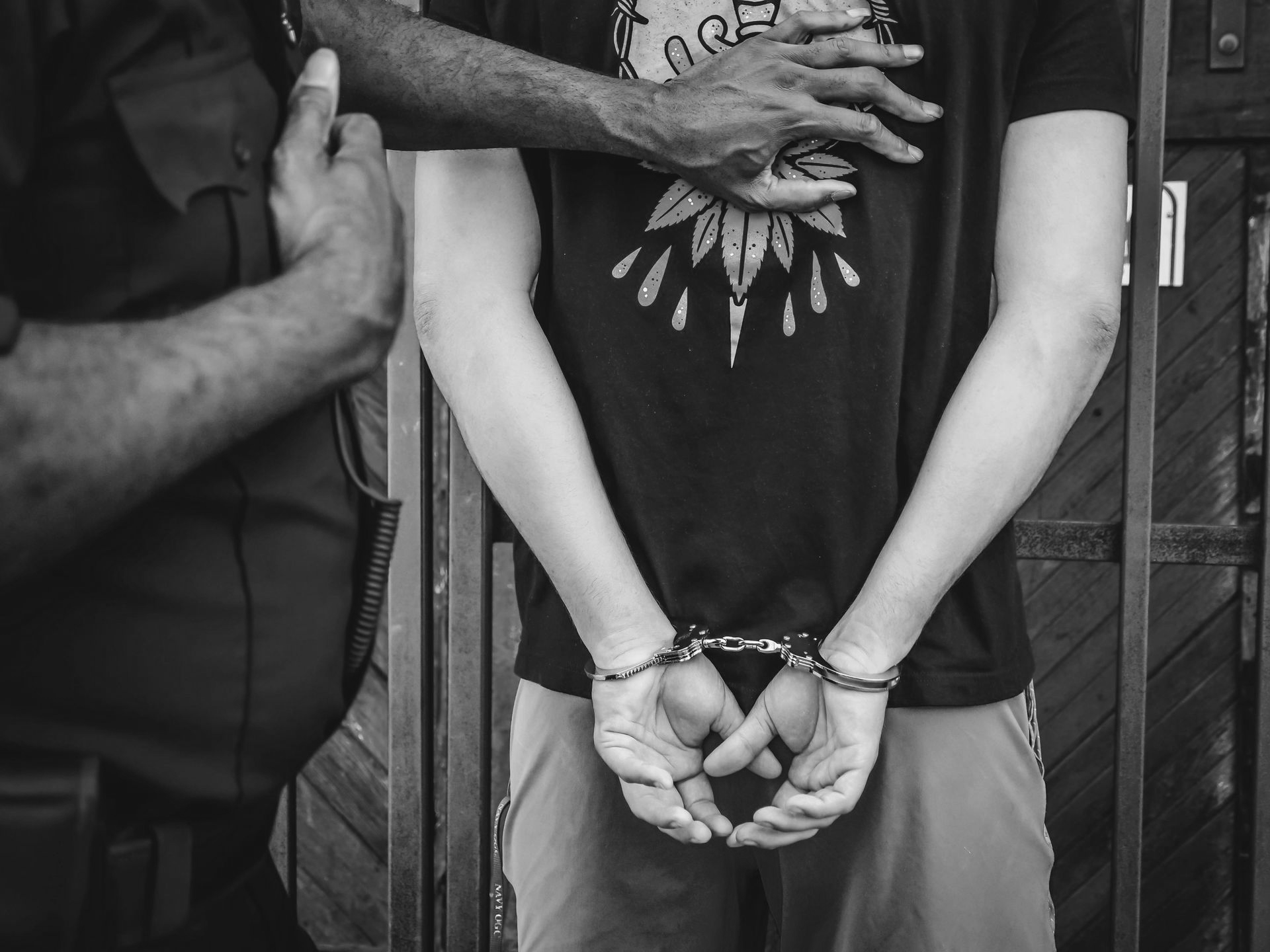 Man in handcuffs, being apprehended by a person in uniform.