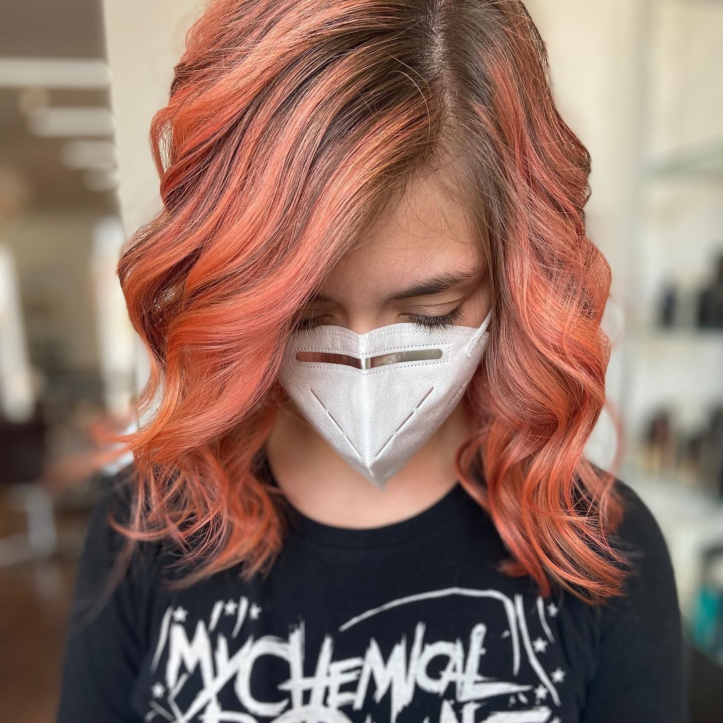 Person with styled coral-colored hair wearing a white face mask, black shirt.