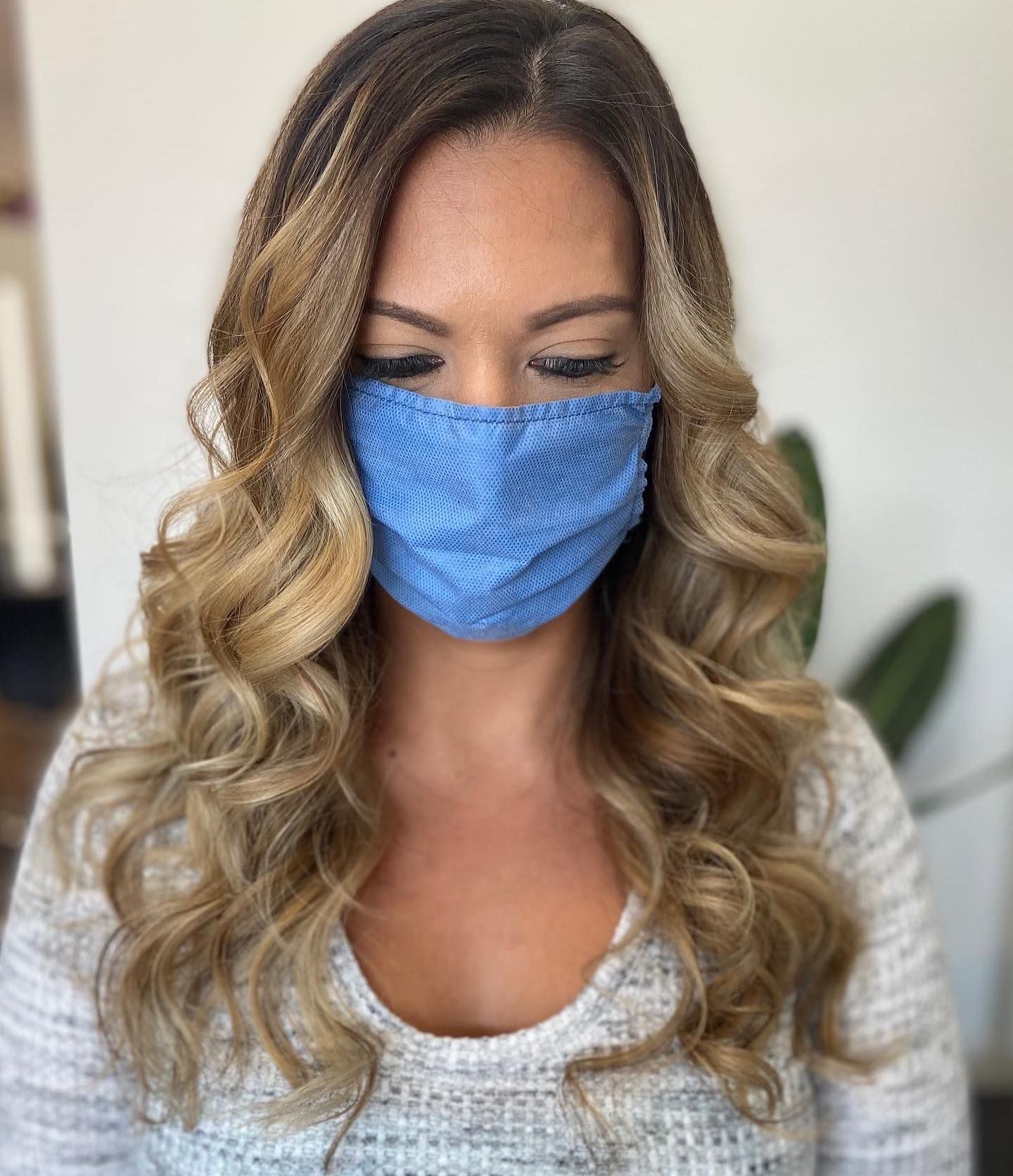 Woman with long, wavy blonde hair, wearing a blue face mask.