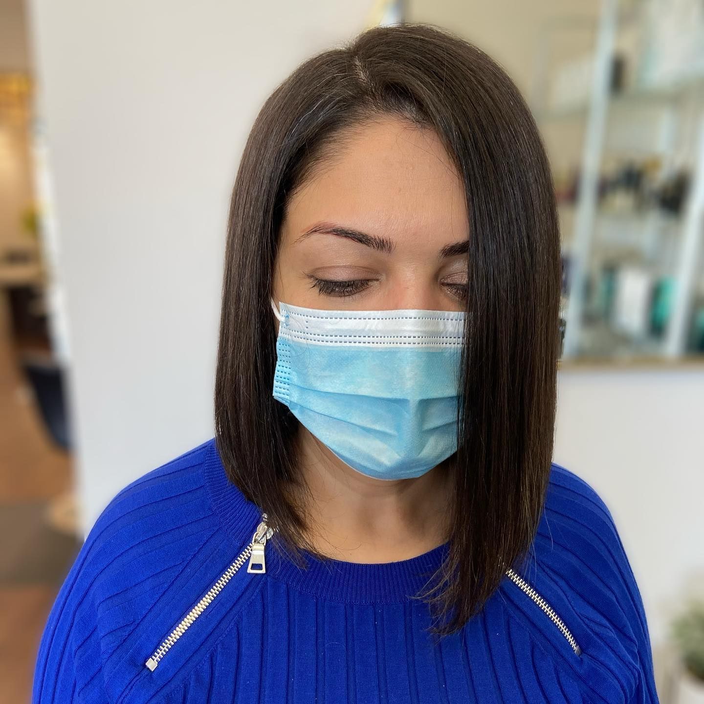 Woman with a blue face mask and a blue sweater, posing indoors.