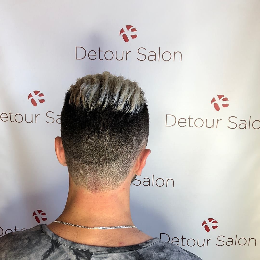 Person's back, undercut hairstyle with dark to blonde color gradient. Detour Salon logo in background.