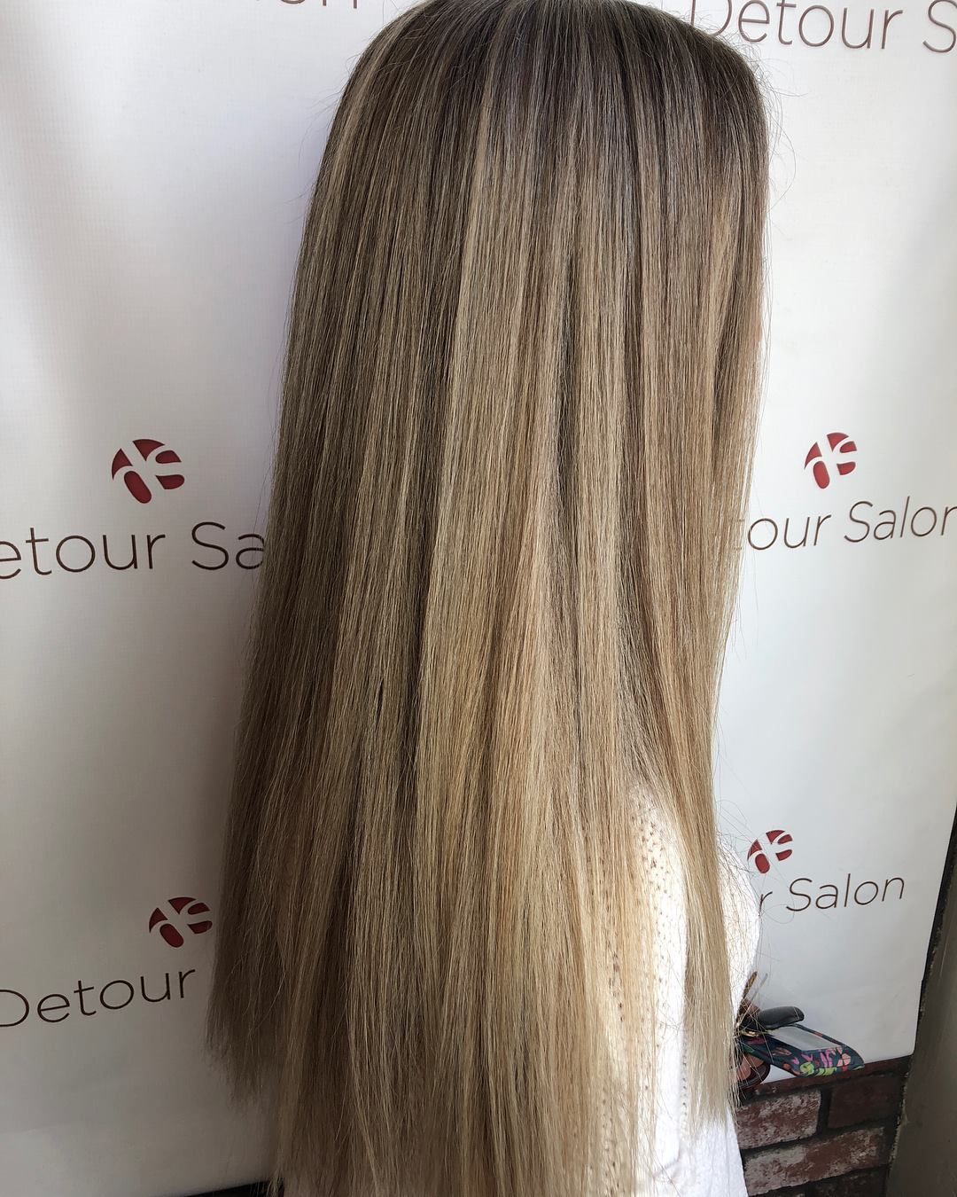 Long, crimped blonde and brown hair, styled straight down. Set against a salon backdrop.