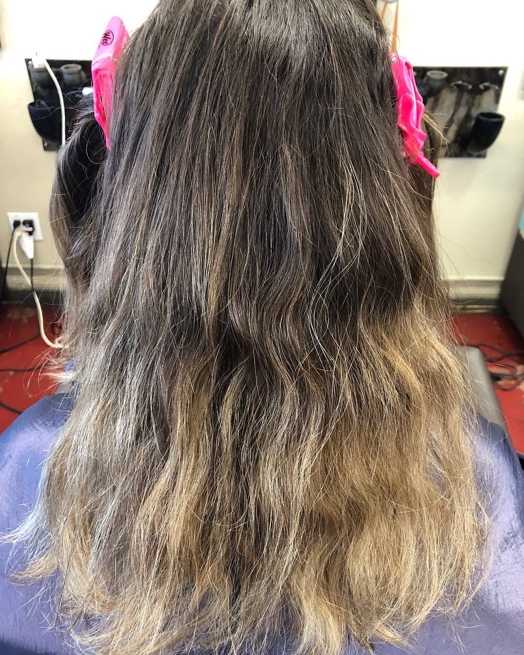 Hair with multiple shades of brown and blonde, in a salon, being prepped for a treatment with pink clips.