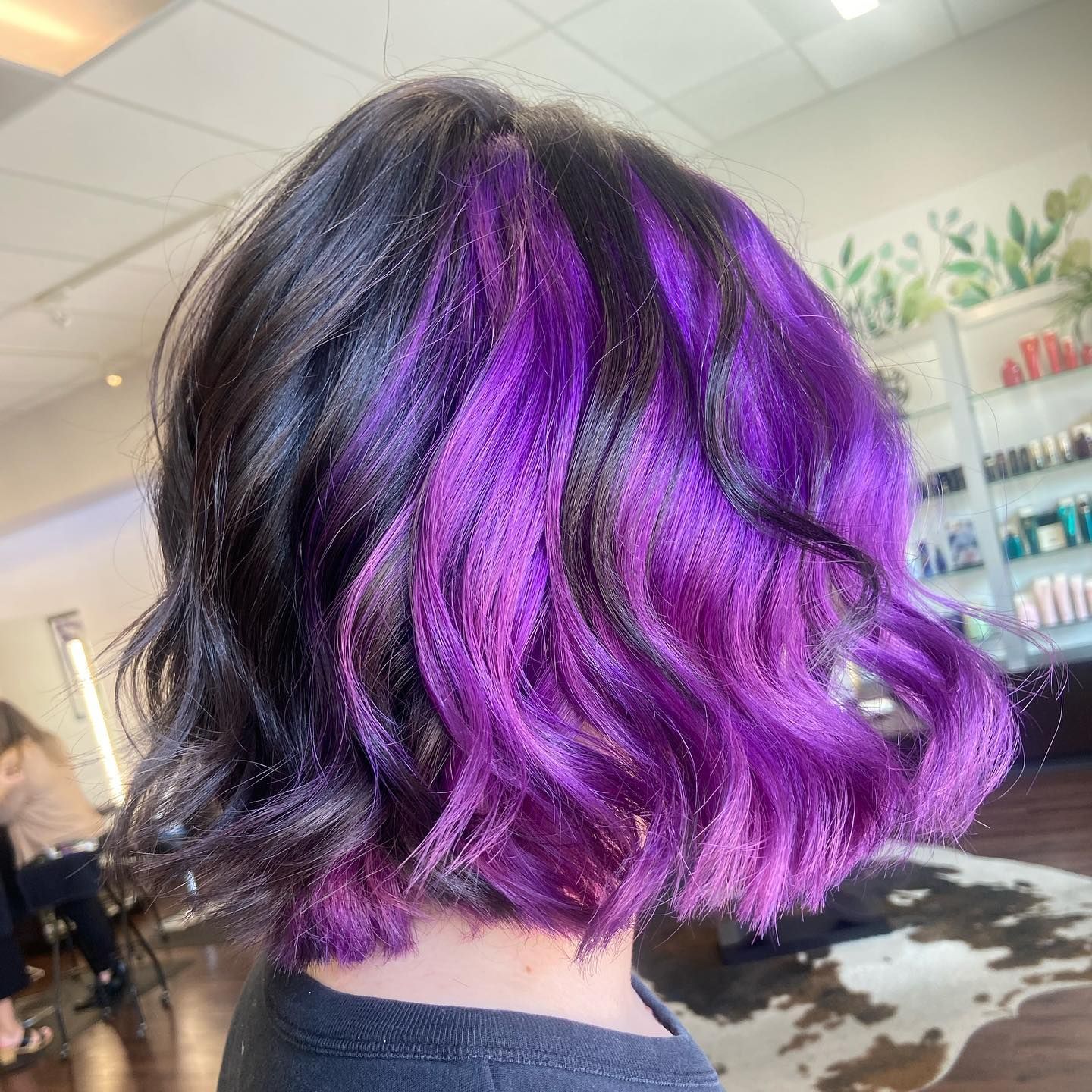 Short, dark hair with vibrant purple sections. Inside a hair salon.