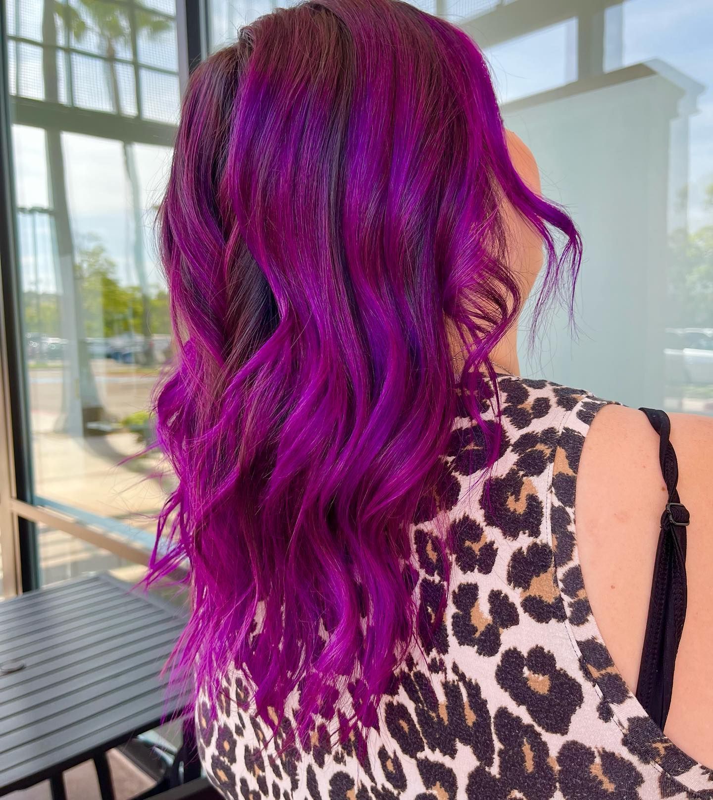 Woman with long, wavy purple hair. Black roots fade to vibrant purple. She wears a leopard print top.