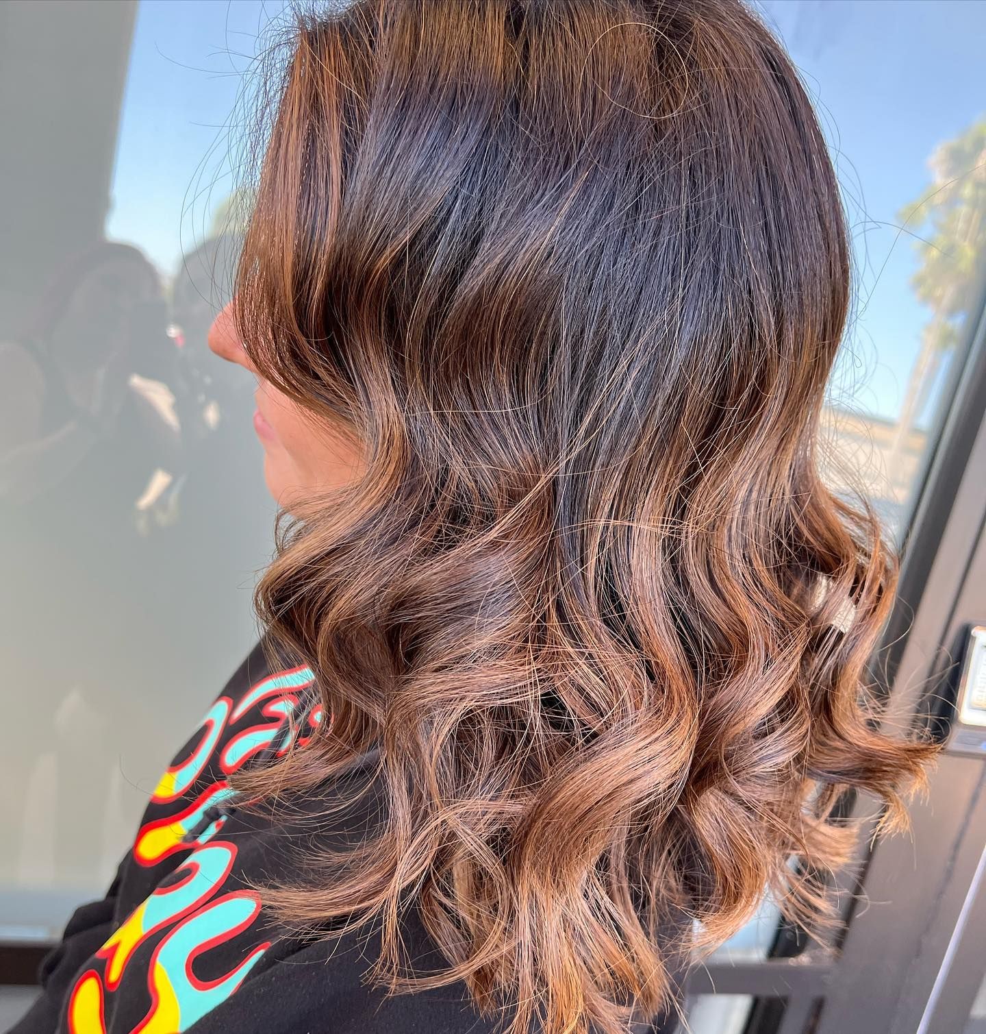 Woman with dark brown hair, lighter brown highlights, styled in waves.