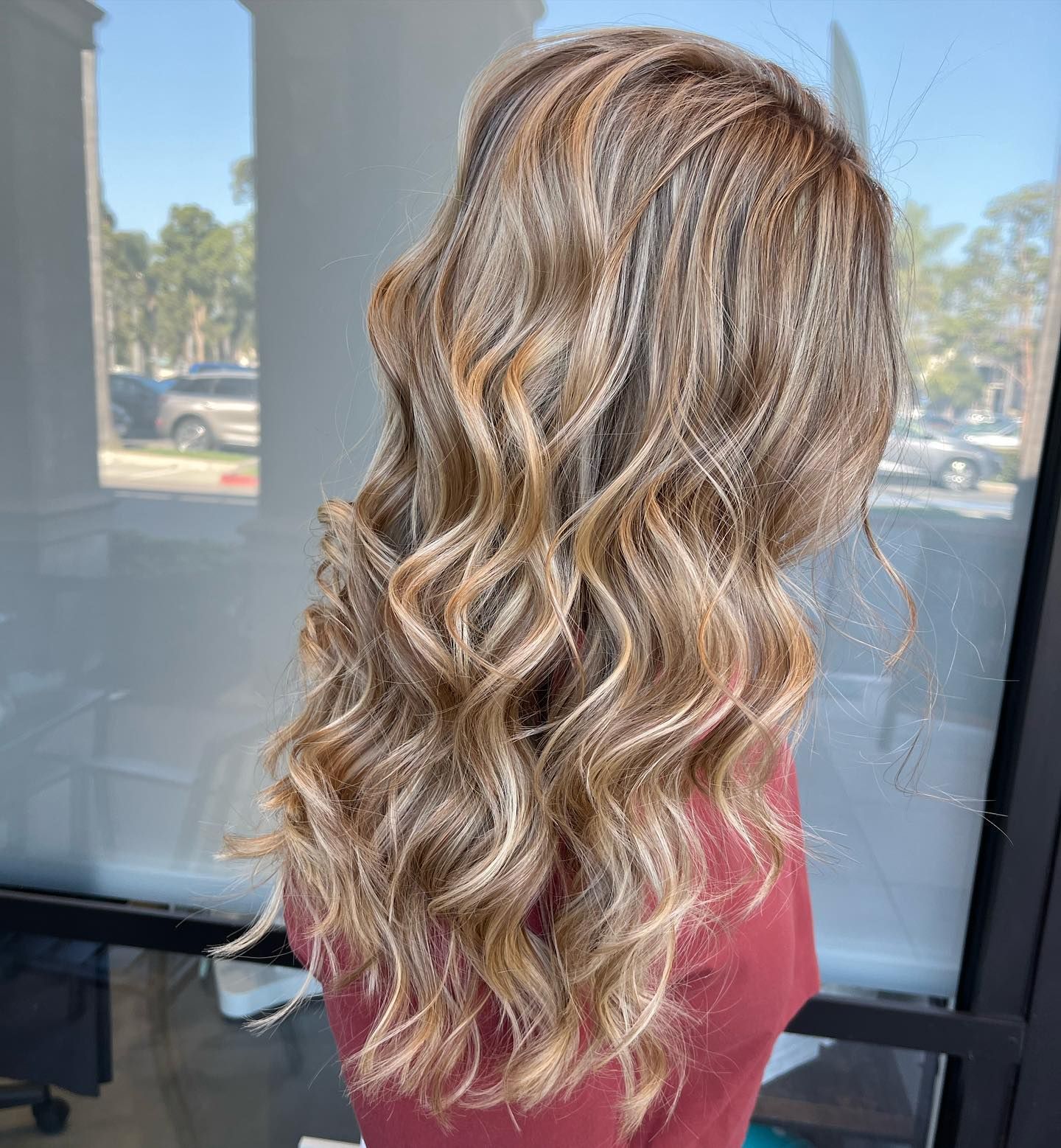 Woman with long, wavy blonde and light brown highlighted hair. Sunlight streams through window.