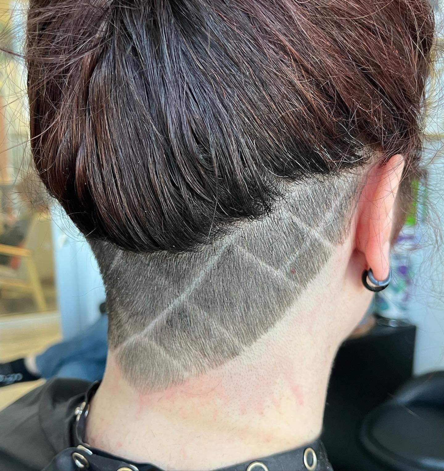 Person with a geometric shaved design at the nape of the neck; hair is pulled up.