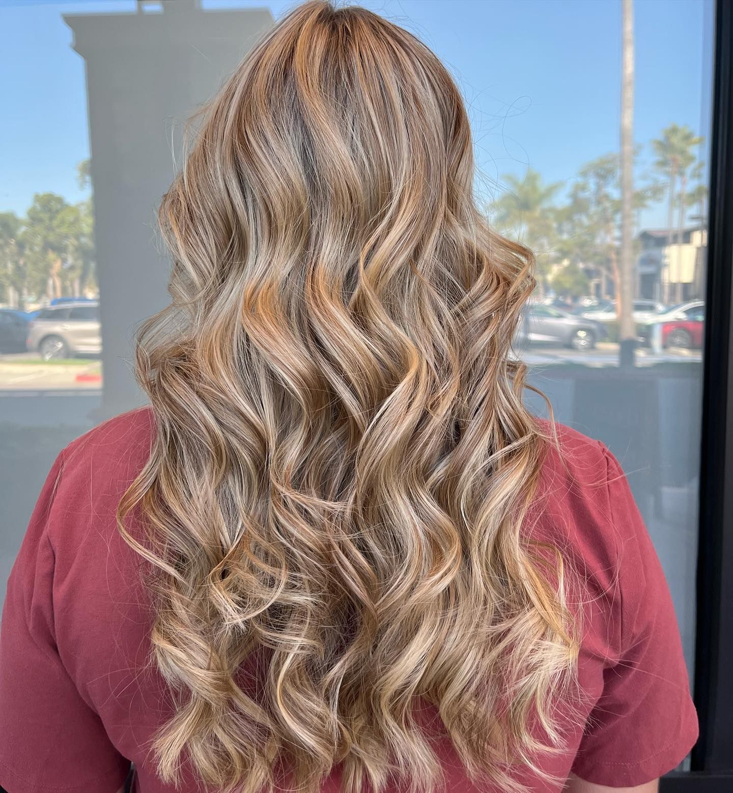 Woman's long wavy hair with blonde highlights. Outdoors, with a red shirt.