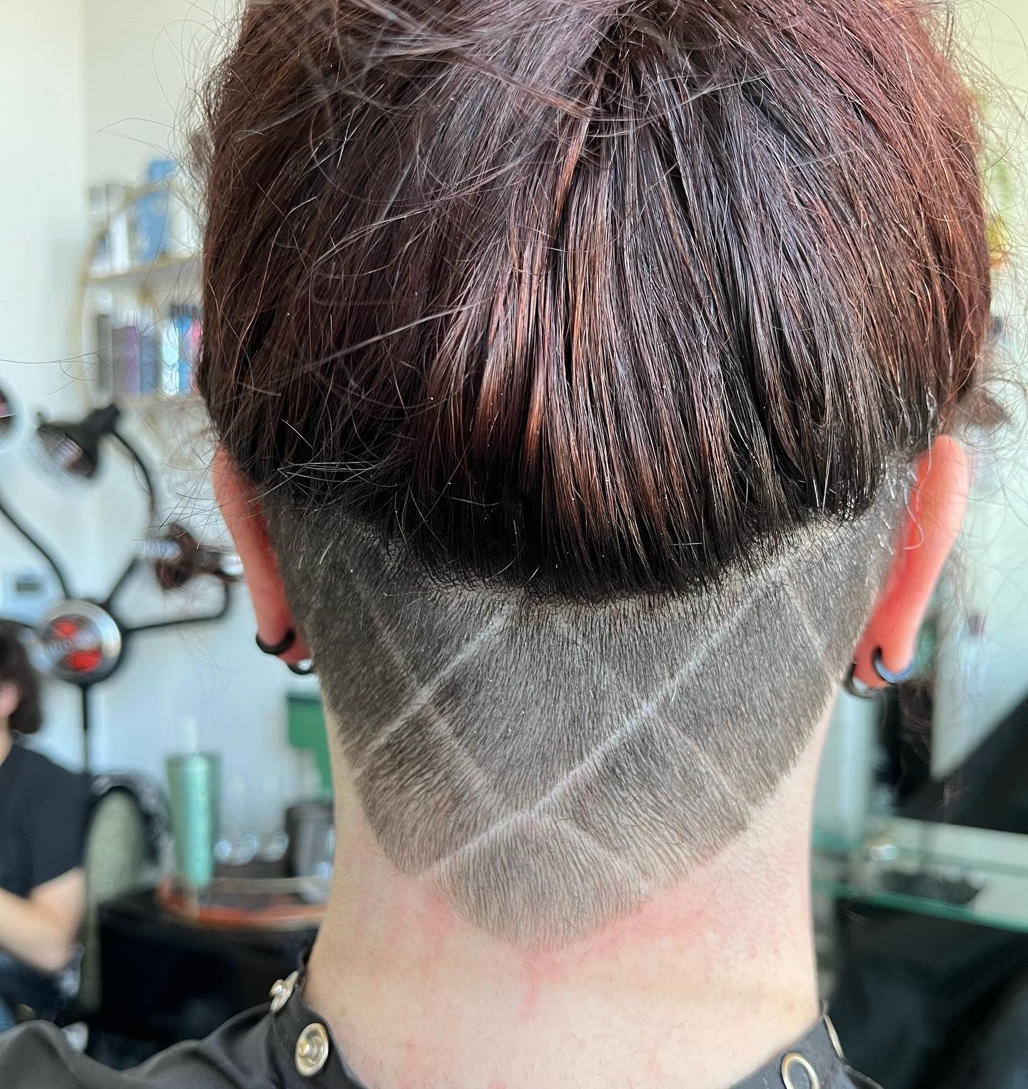 Back of a person's head with a geometric shaved design. Dark brown hair with a faded pattern above the neck.