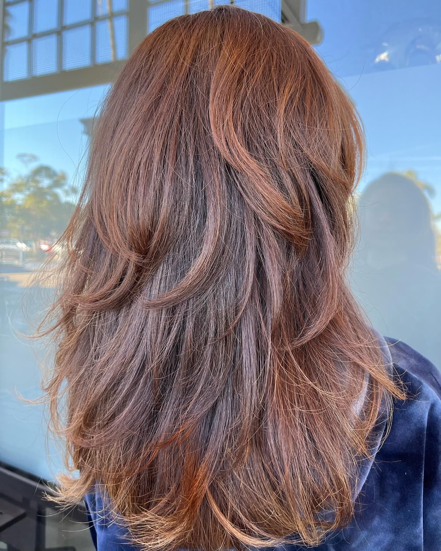 Woman with layered, reddish-brown hair in front of a window.
