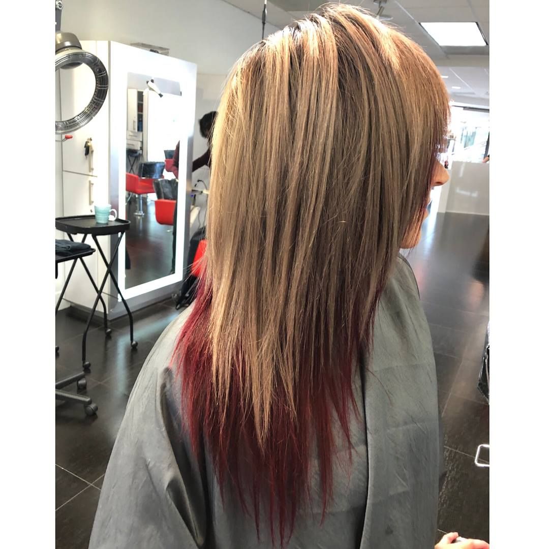 Person with long, layered blonde hair with red dip-dyed ends in a salon.