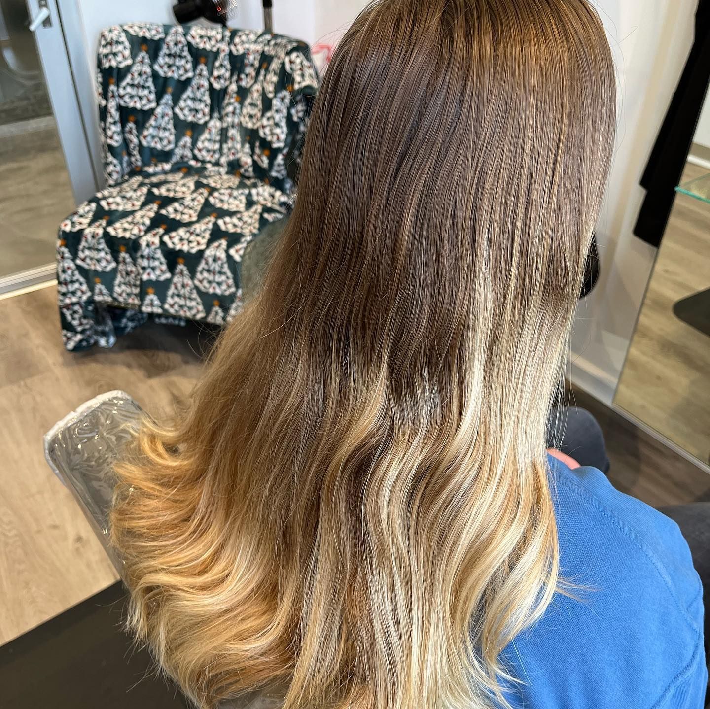 Woman with wavy ombre hair, dark roots to blonde tips. Sitting in a salon chair.