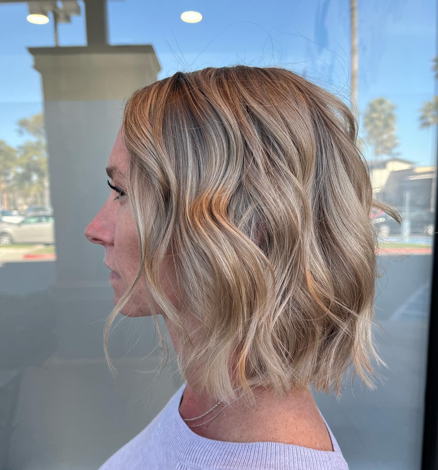 Woman with wavy blonde bob hairstyle, standing outside.