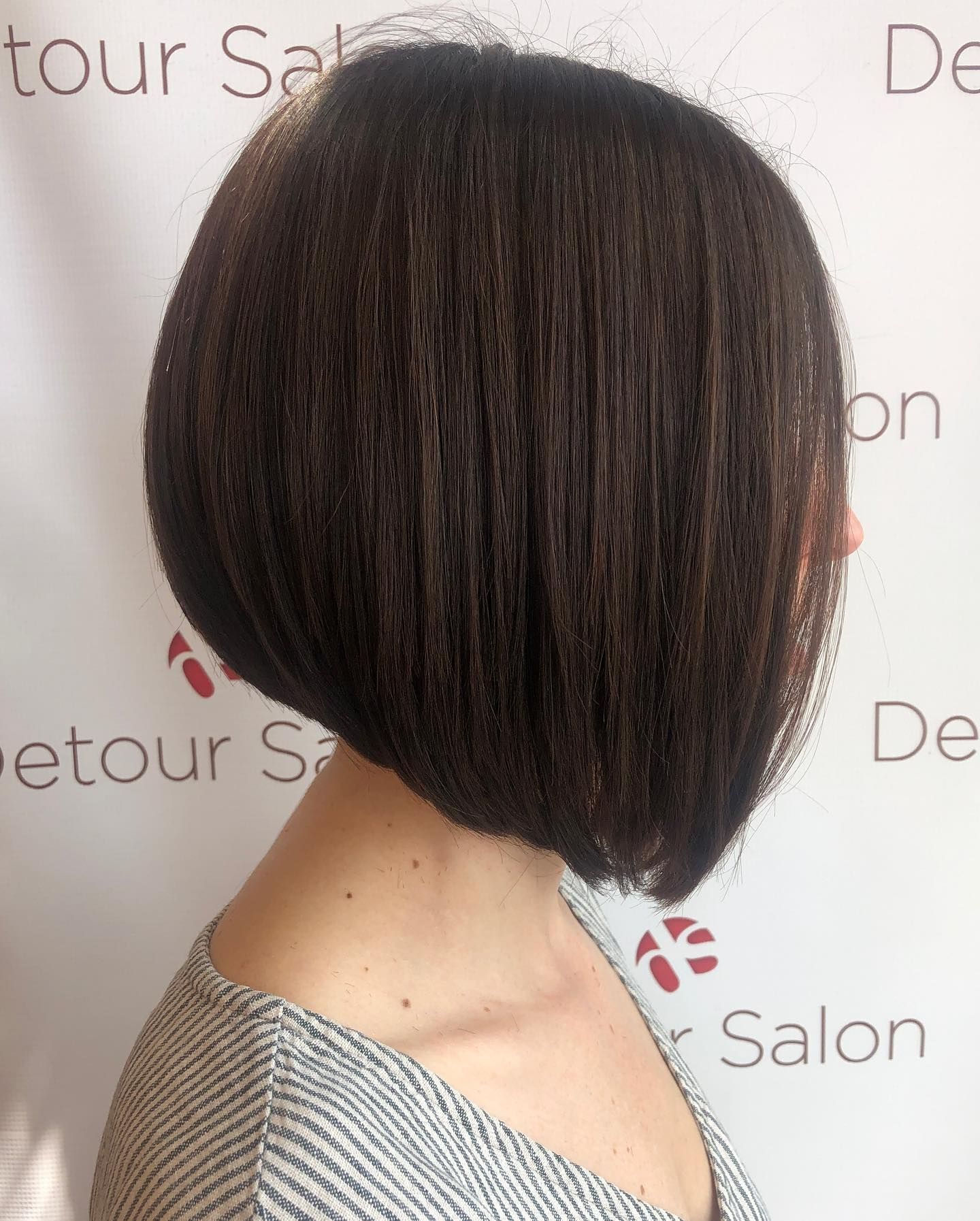 Woman's dark brown bob hairstyle, angled towards the face. She wears a gray and white striped top.