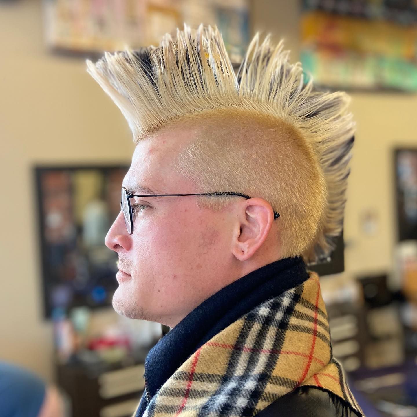 Man with a blonde mohawk and glasses, wearing a scarf in a salon setting.