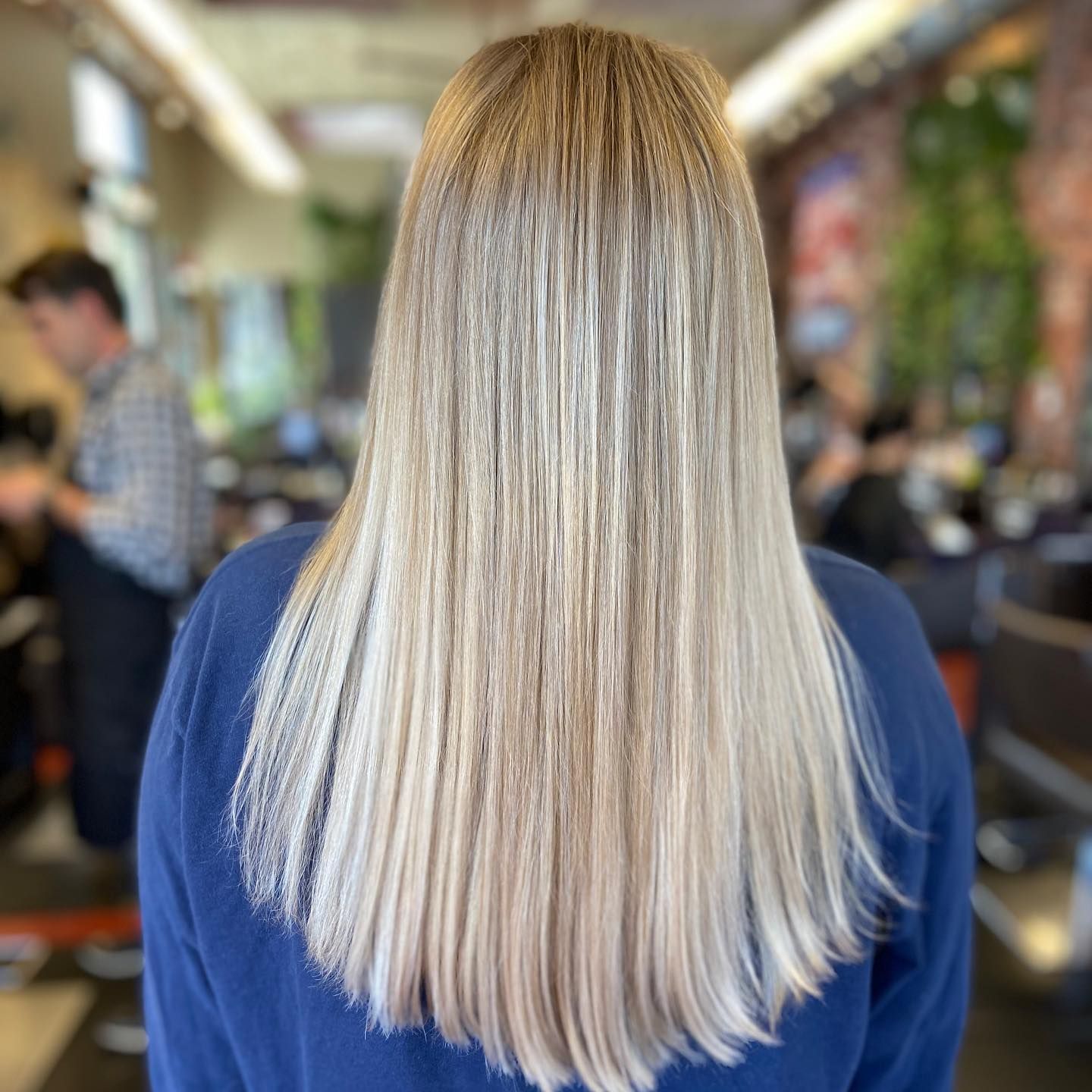Woman with long, straight, blonde hair at a salon, wearing a blue sweater.