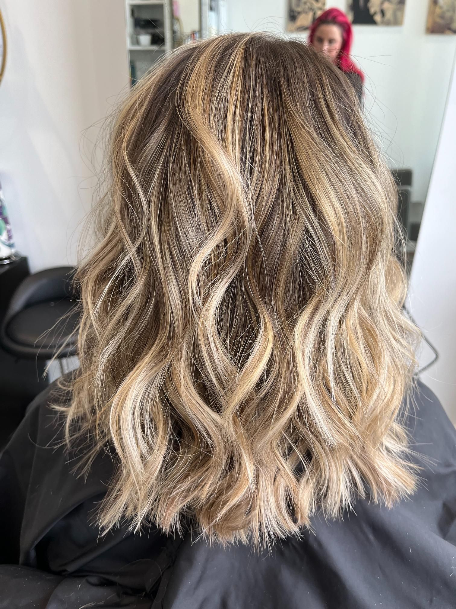 Woman with wavy, highlighted brown and blonde hair. In a salon setting.