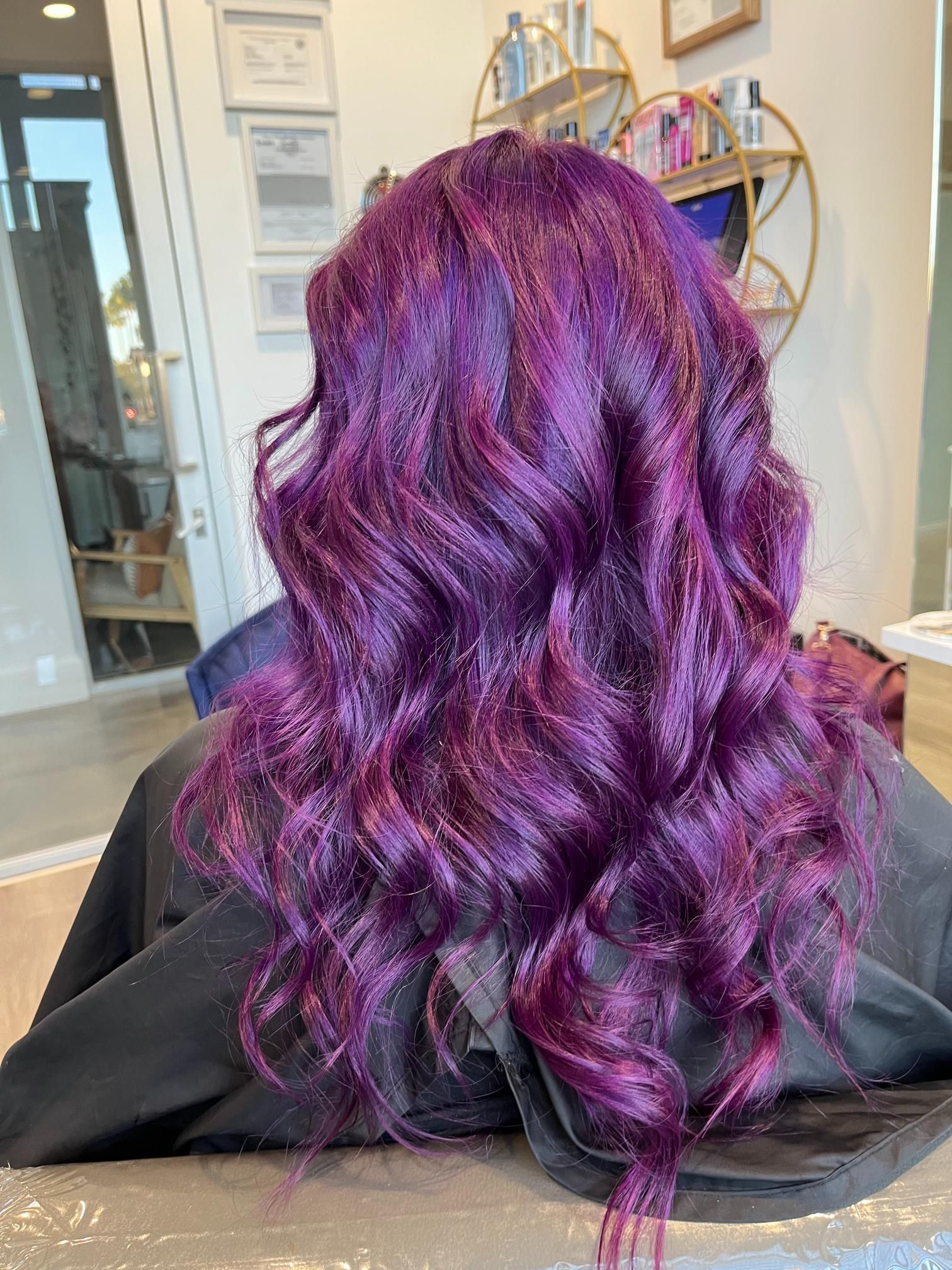 Woman's long wavy hair colored a vibrant shade of purple, set in a salon.
