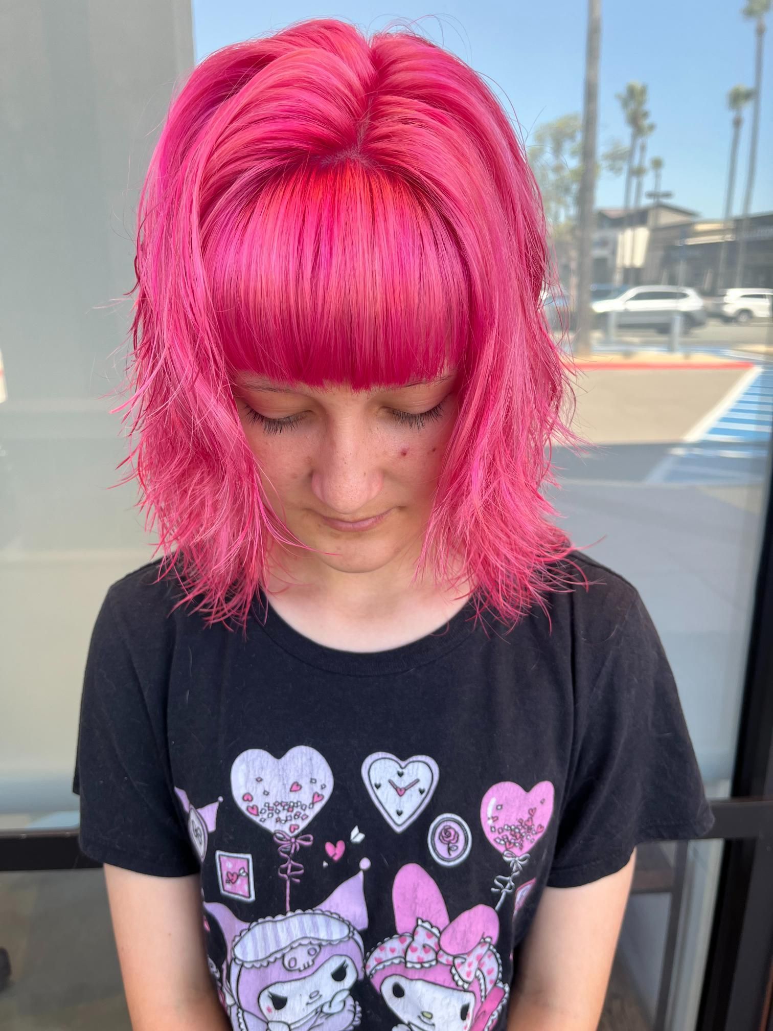 Person with vibrant pink hair and bangs, wearing a black graphic tee, outdoors.