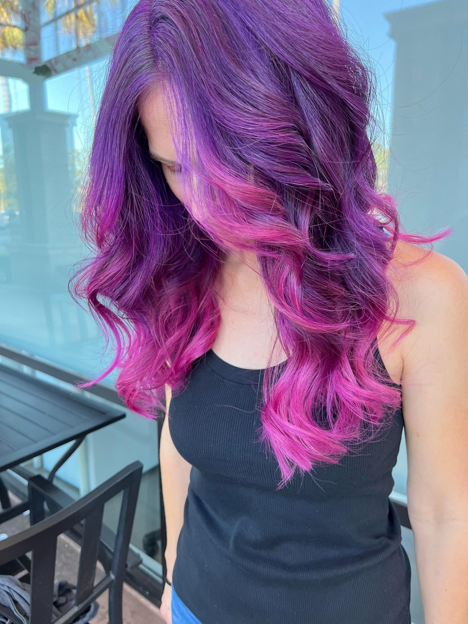 Woman with long, wavy purple and pink hair, wearing a black tank top, outdoors.
