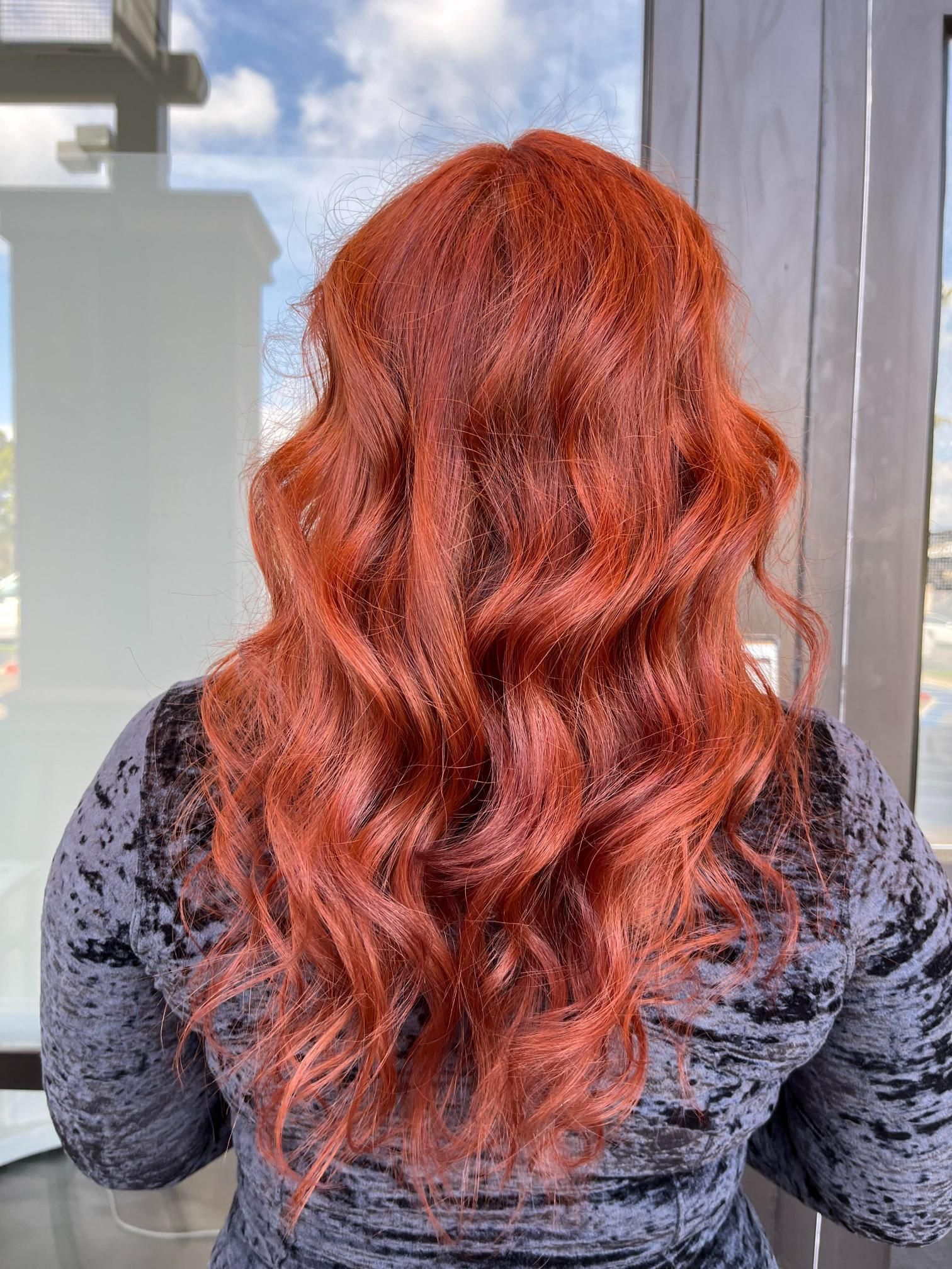 Person with long, wavy, fiery red hair against a bright background, wearing a dark velvet top.